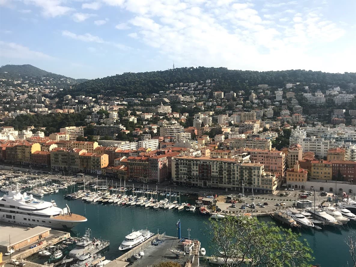 Scenic harbor view in Nice, France, featuring colorful boats and the stunning Mediterranean coastline in the background.