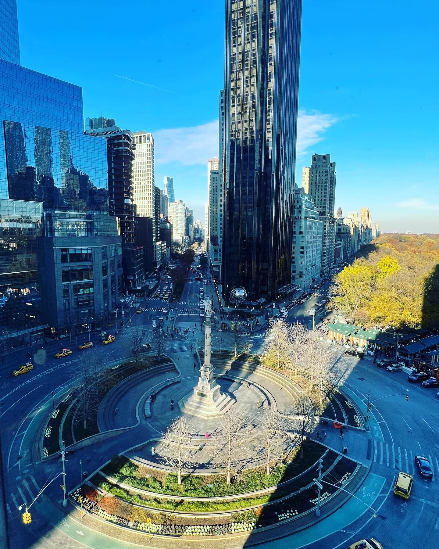 A bustling city street featuring a central fountain surrounded by pedestrians and buildings, showcasing urban life.
