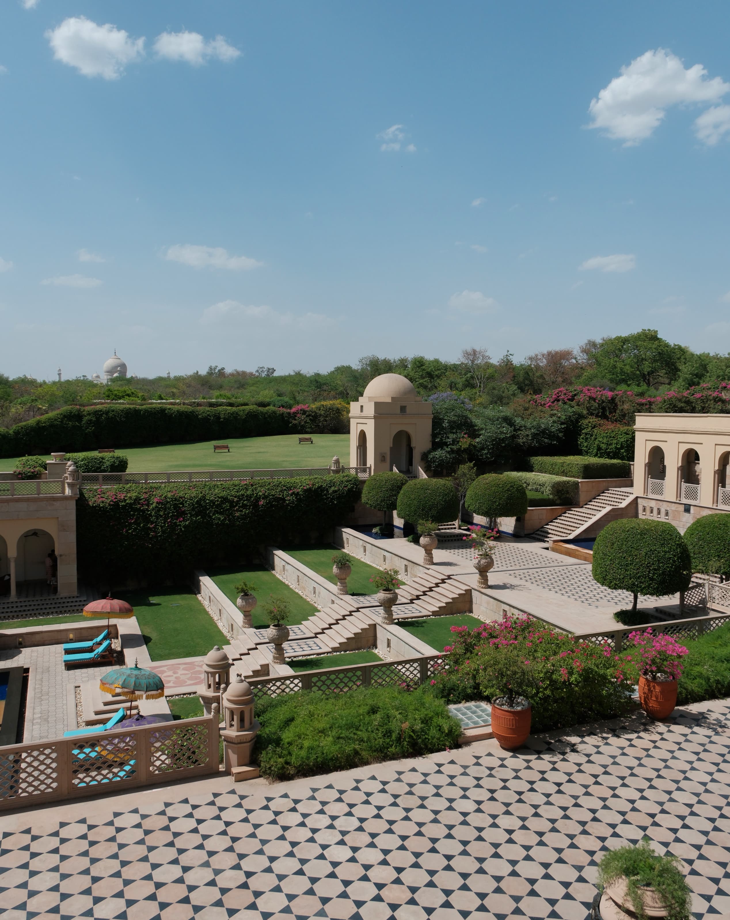 A view of a terrace with beautiful mosaic tiling, manicured landscaping, stone domes and archways and a beautiful field in the distance. 