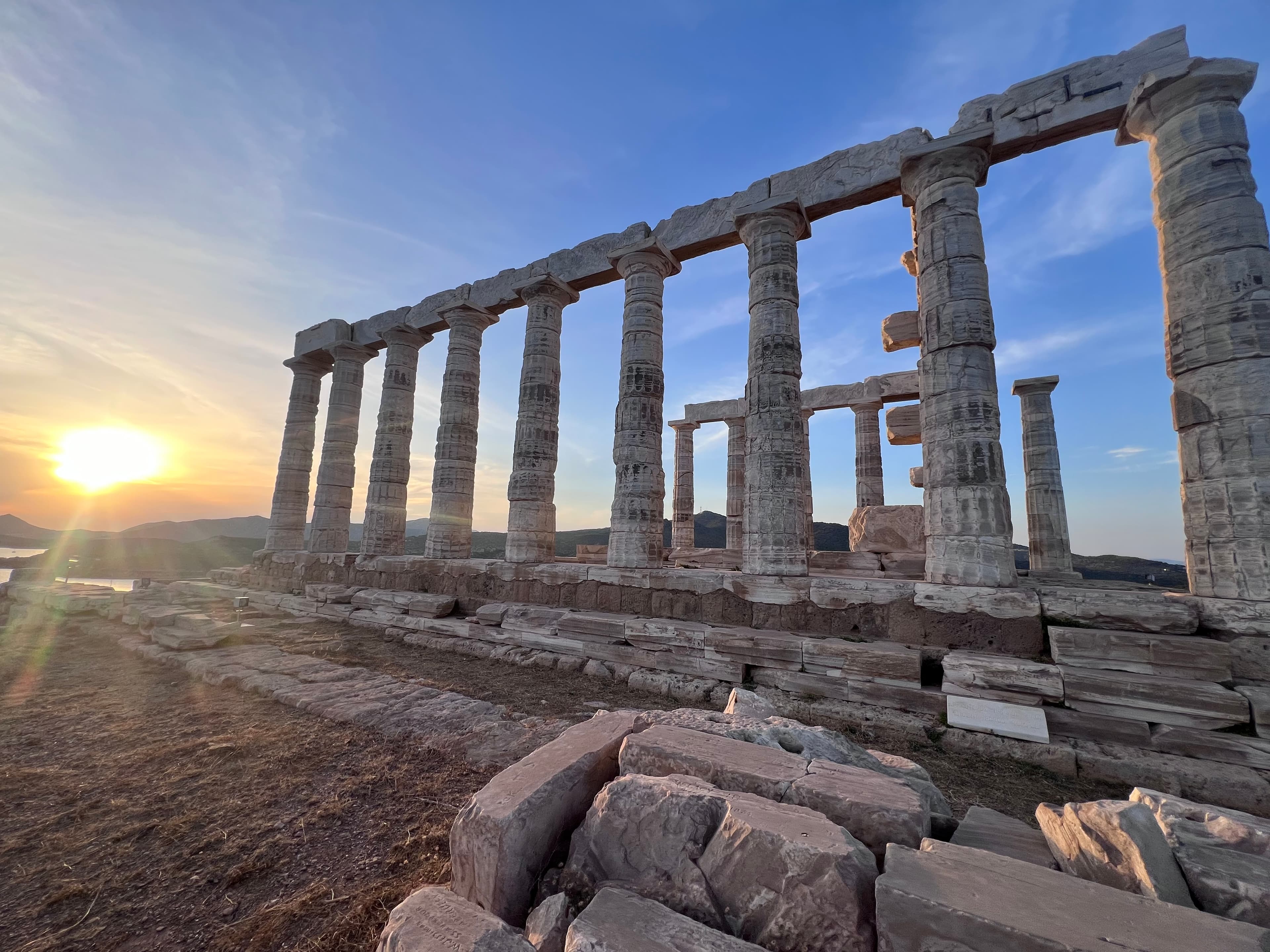 A breathtaking sunset casts a warm glow over the ruins of an ancient Greek temple.