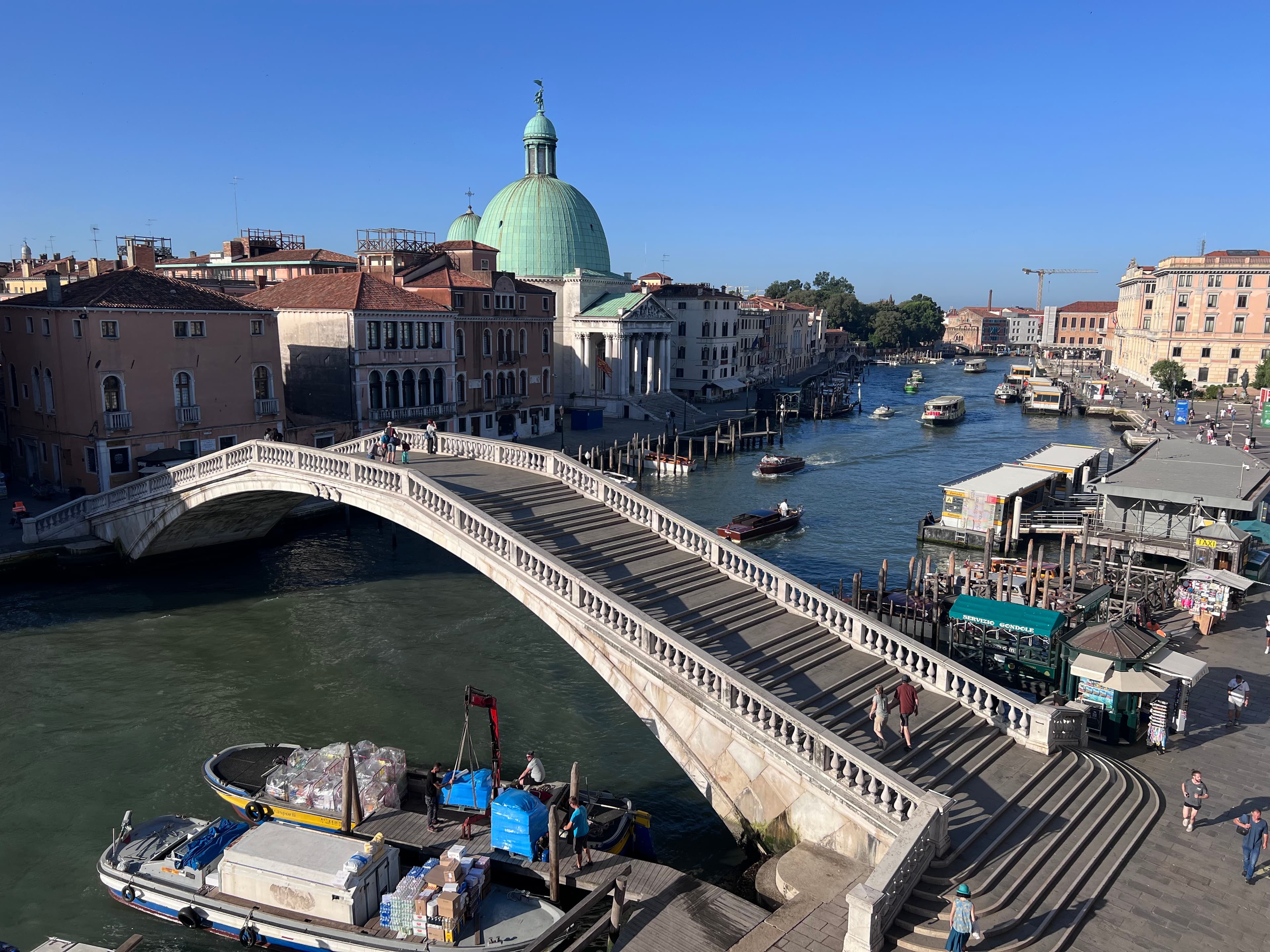 A scenic view of a bridge spanning across a tranquil river, surrounded by lush greenery and clear blue skies.