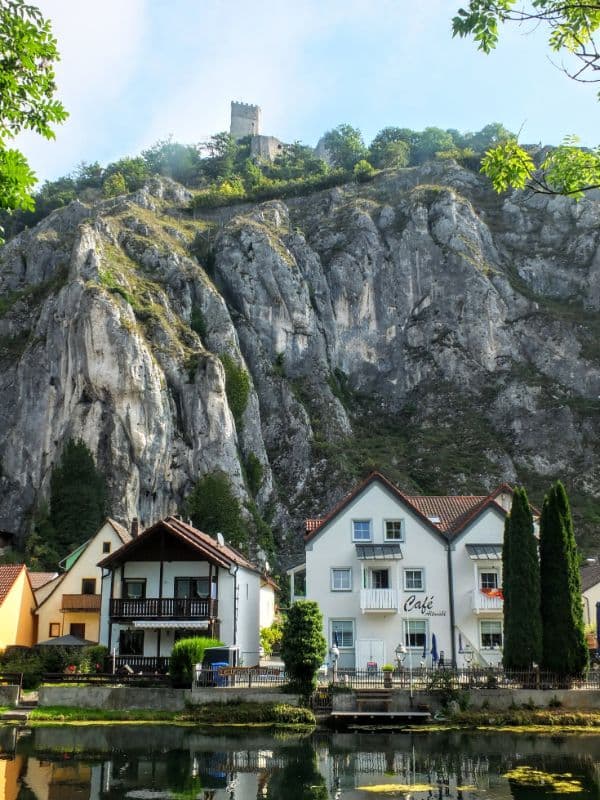 A view of two quaint homes on the coastline at the based of a large mountain during the day.