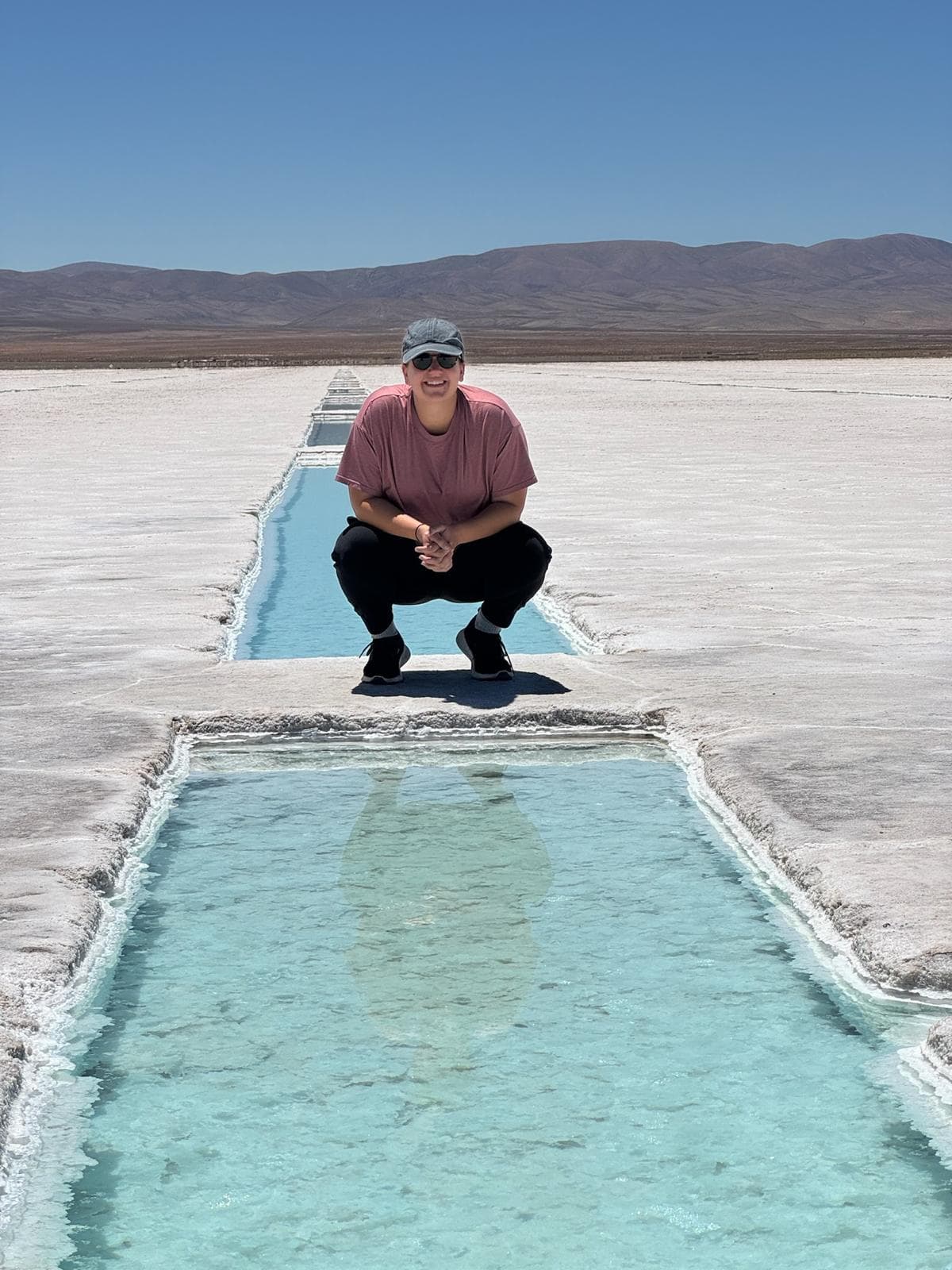 Advisor crouching before a rectangular body of water surrounded by salt flats on a sunny day