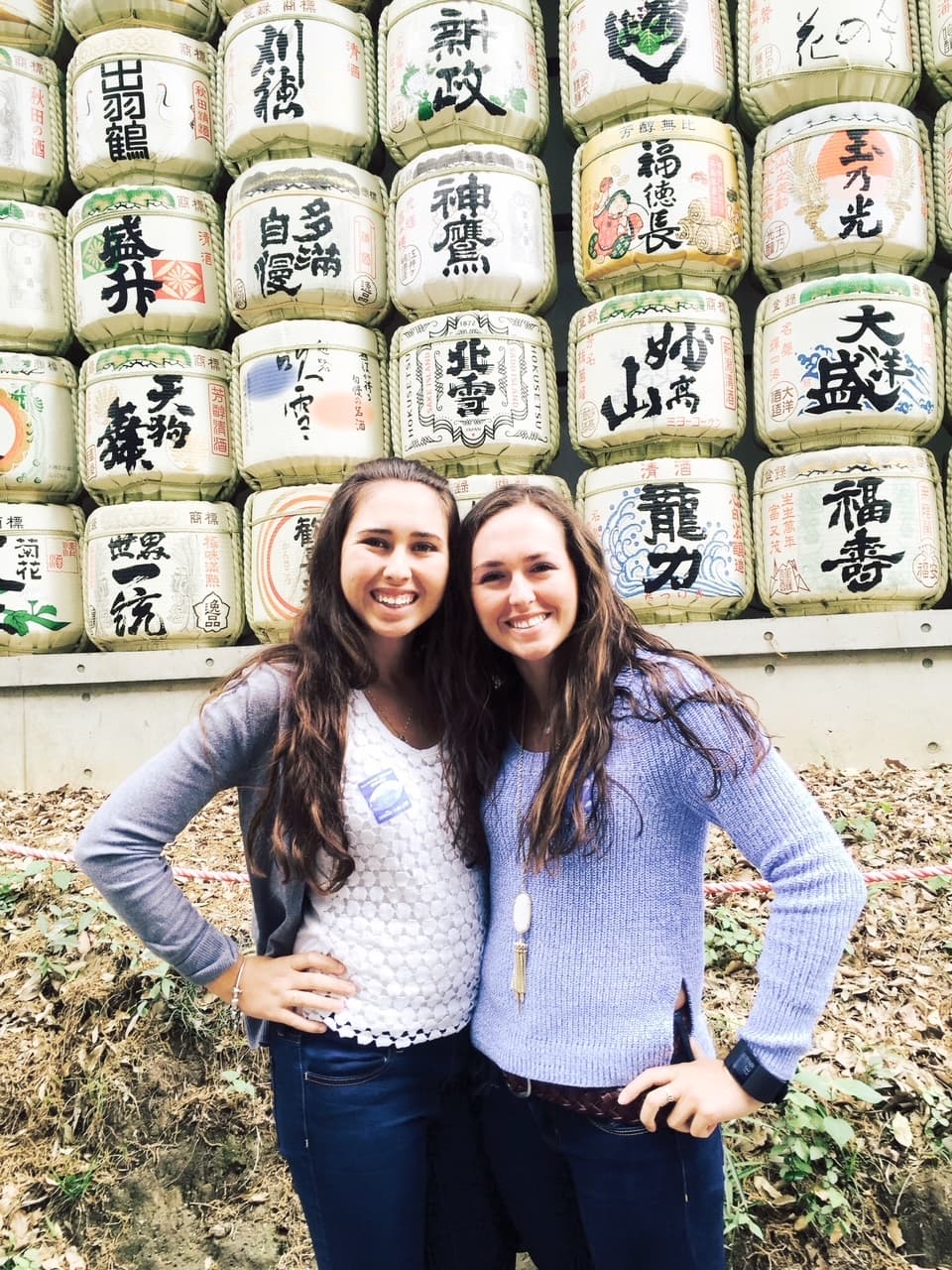 Anna and friend posing side by side in front of a wall with Japanese characters painted on white blocks
