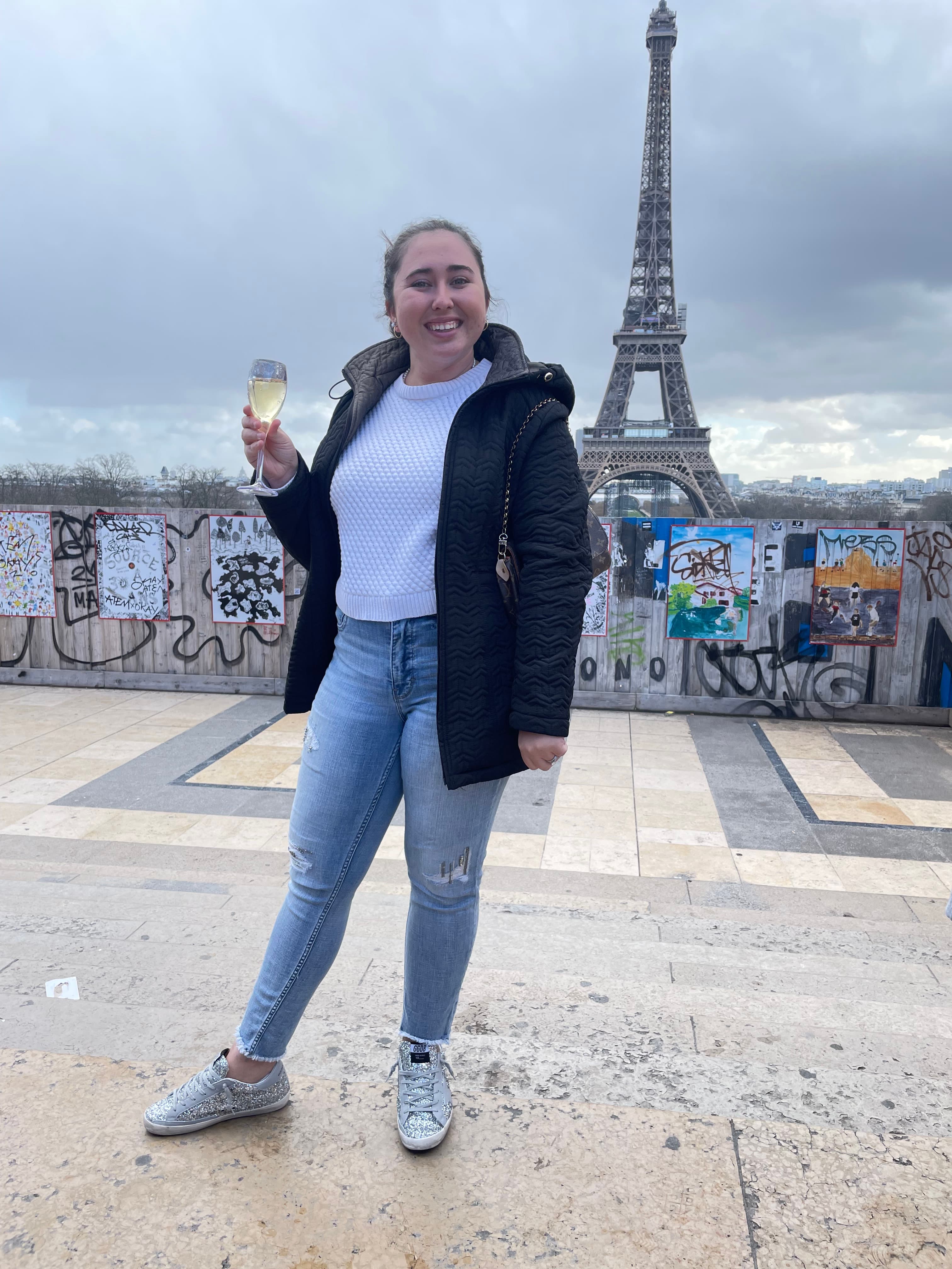 Advisor holding a glass of wine in front of the Eiffel Tower on a cloudy day
