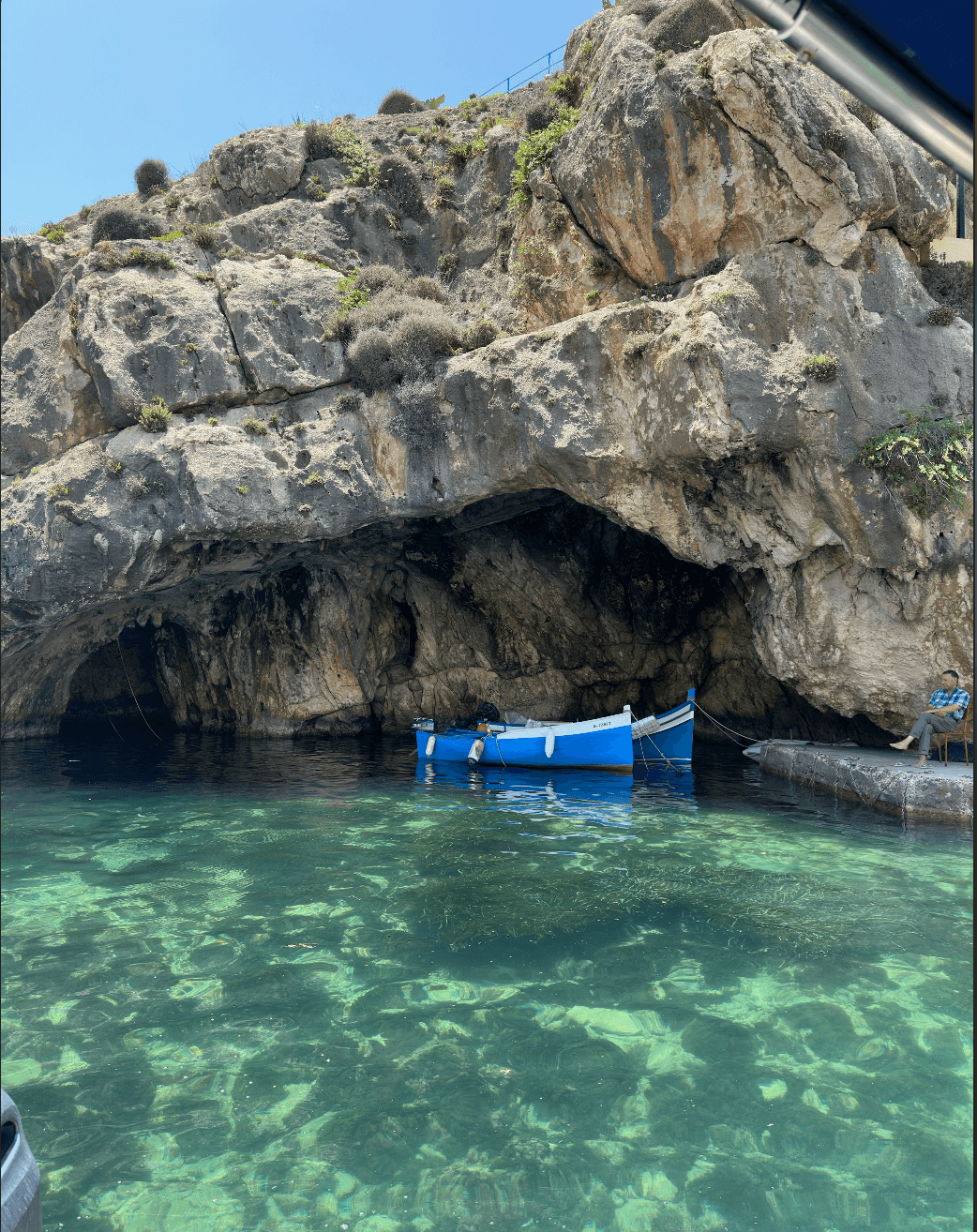 Crystal clear water and a rock formation with two small blue boats docked underneath 
