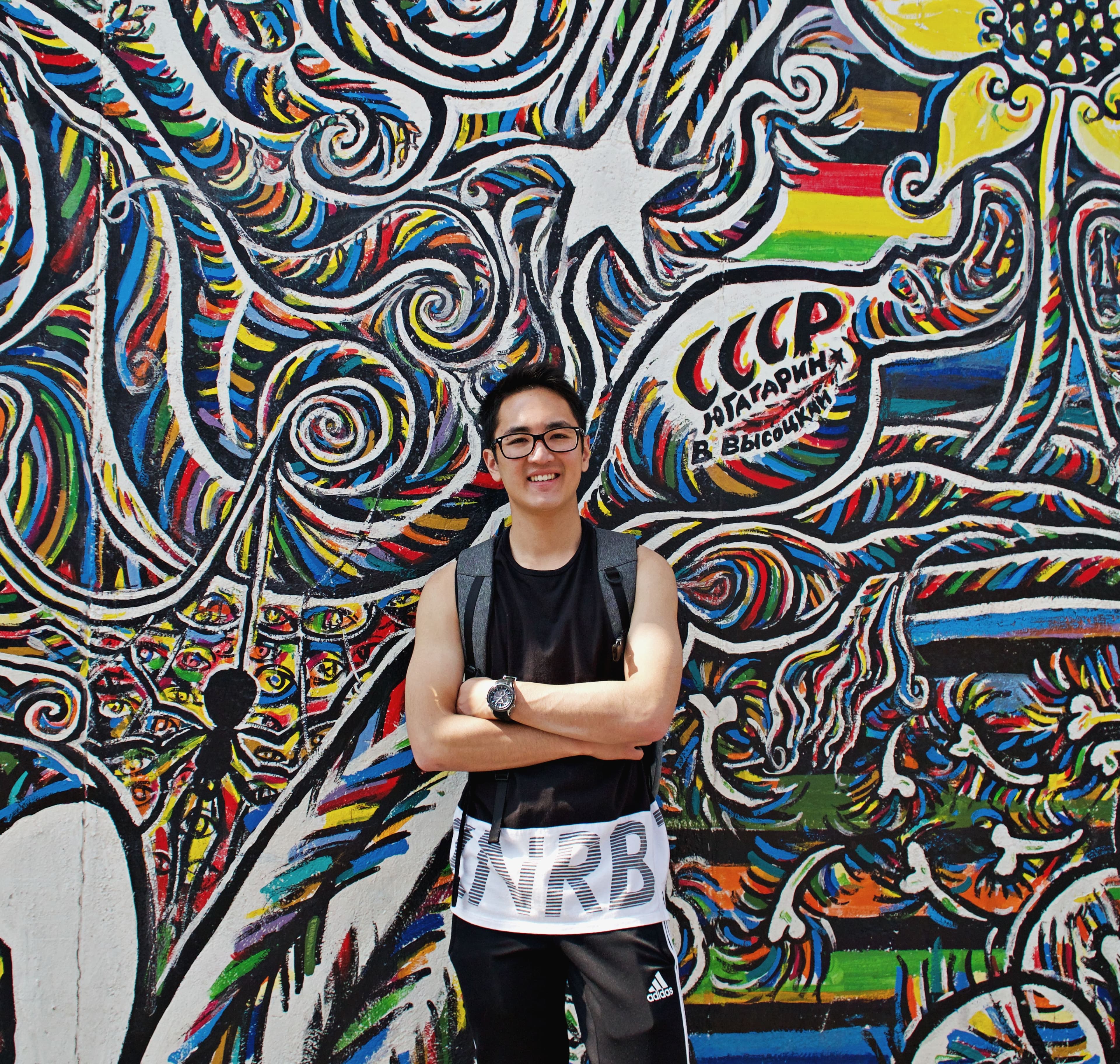 Advisor posing with arms crossed in front of a colorful wall mural on a sunny day