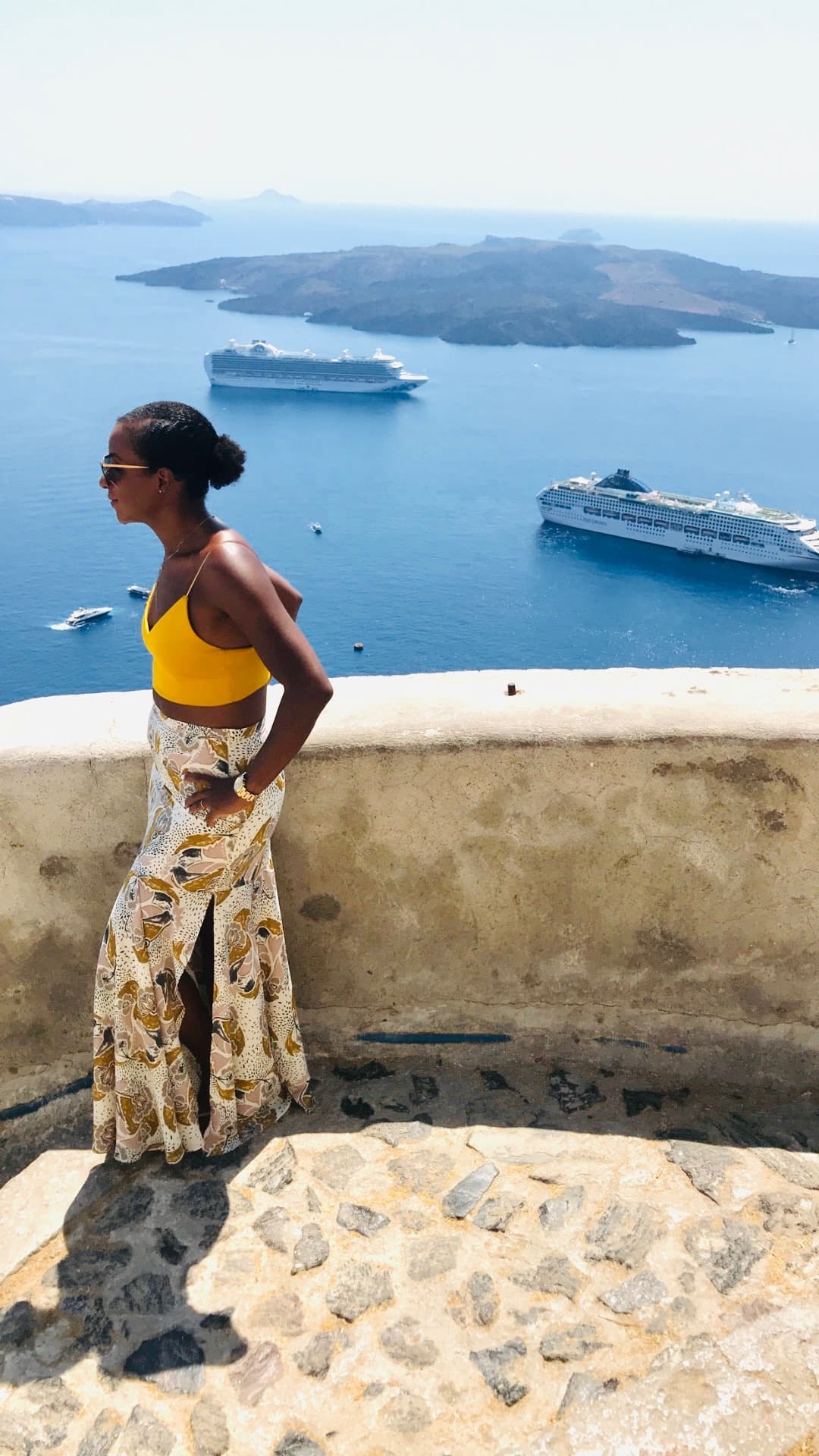 Advisor posing beside a stone wall overlooking the sea with two cruise ships visible offshore
