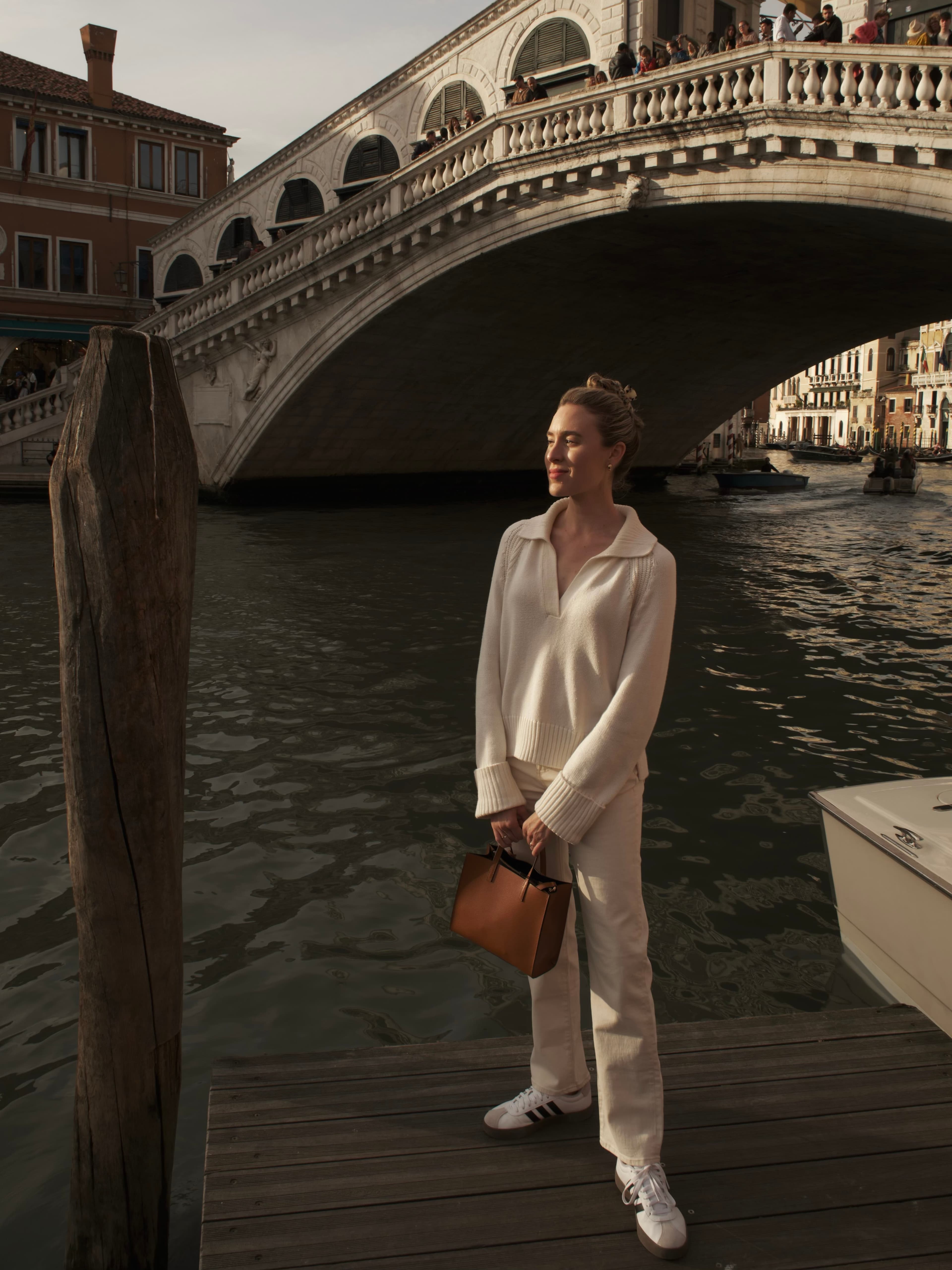 Advisor holding a purse and posing underneath a large bridge in Venice, Italy at sunset