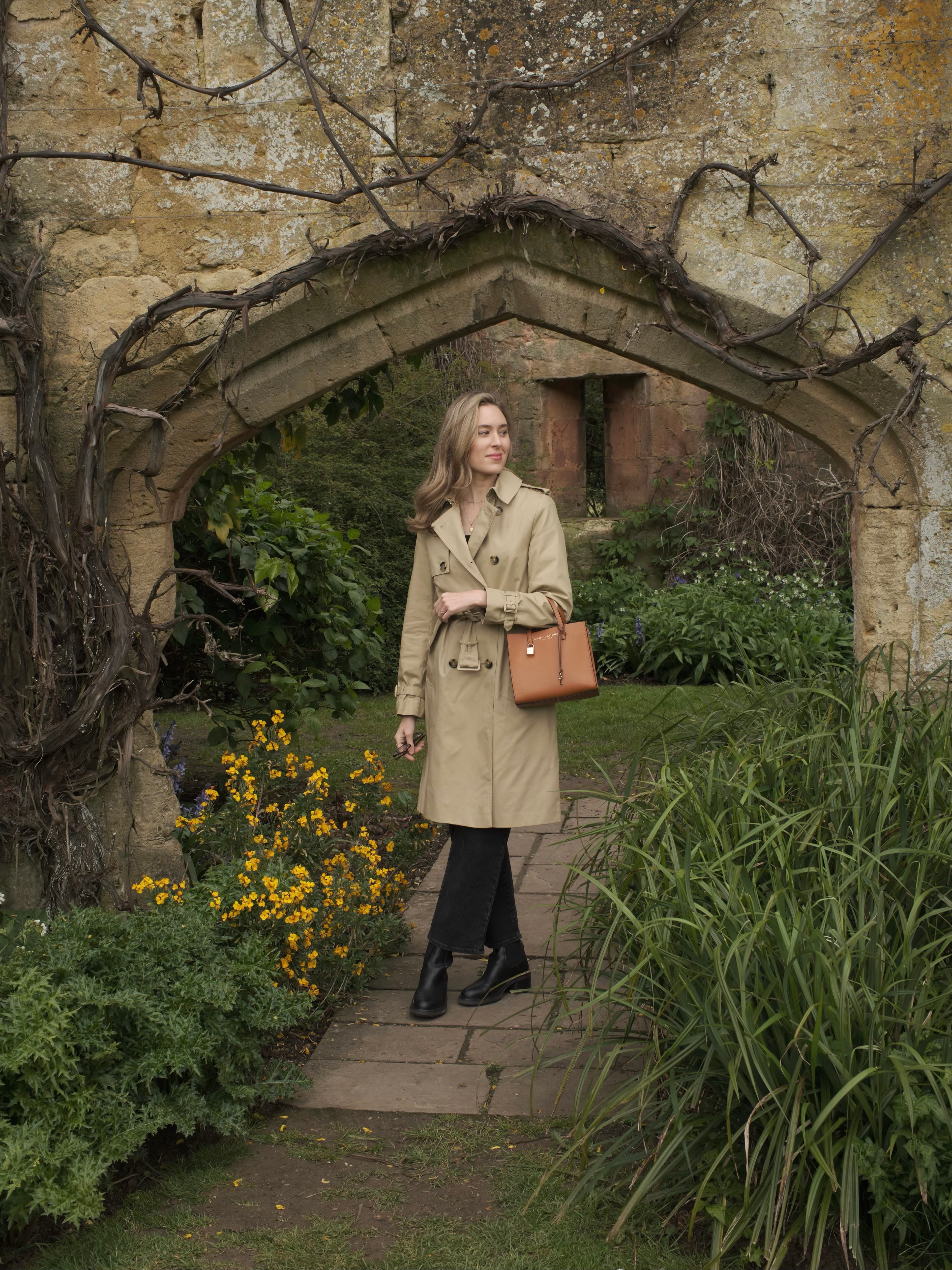View of advisor in a beige trench coat walking through a small garden in the Cotswolds