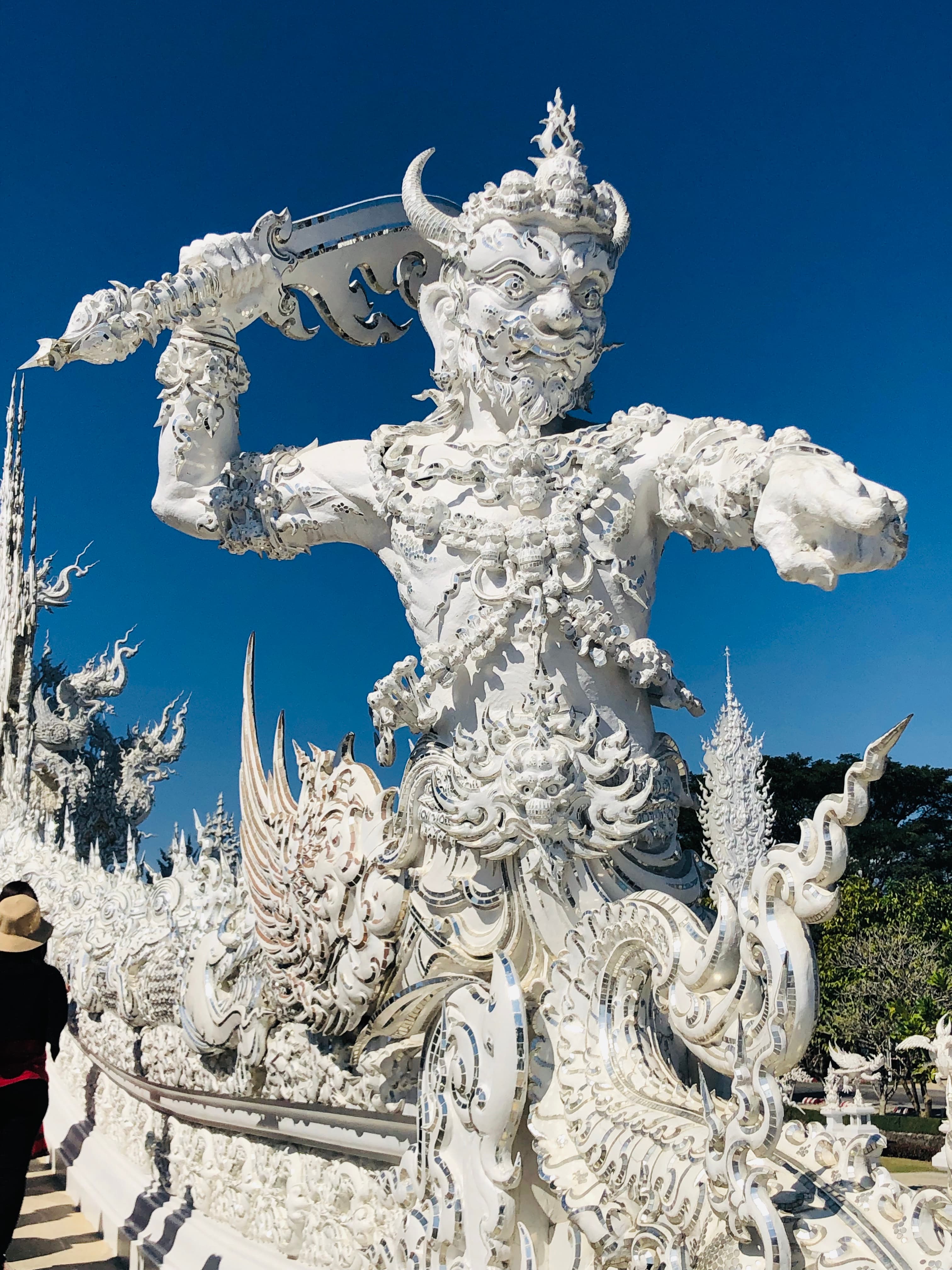 Large white statue of a man/beast warrior at a temple under clear skies