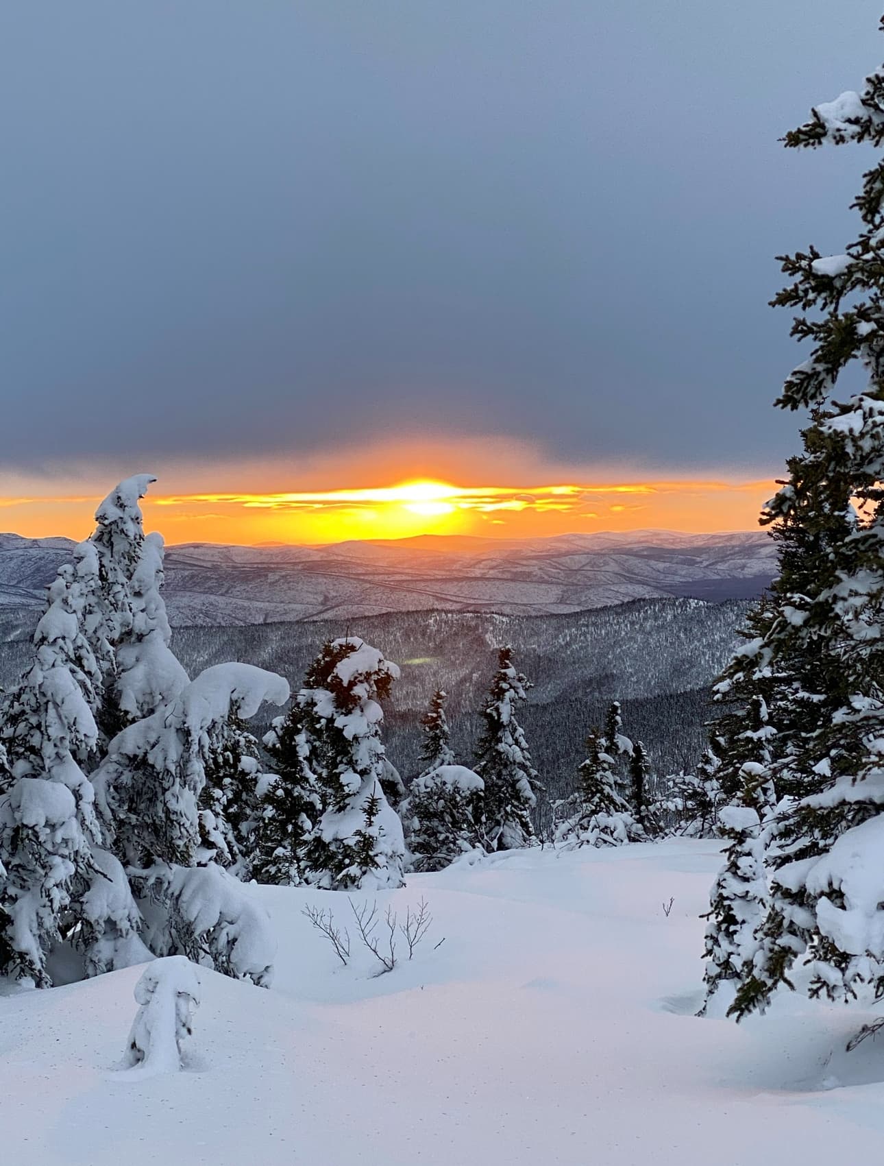View of a bright orange sunset as seen from the top of a snowy mountain