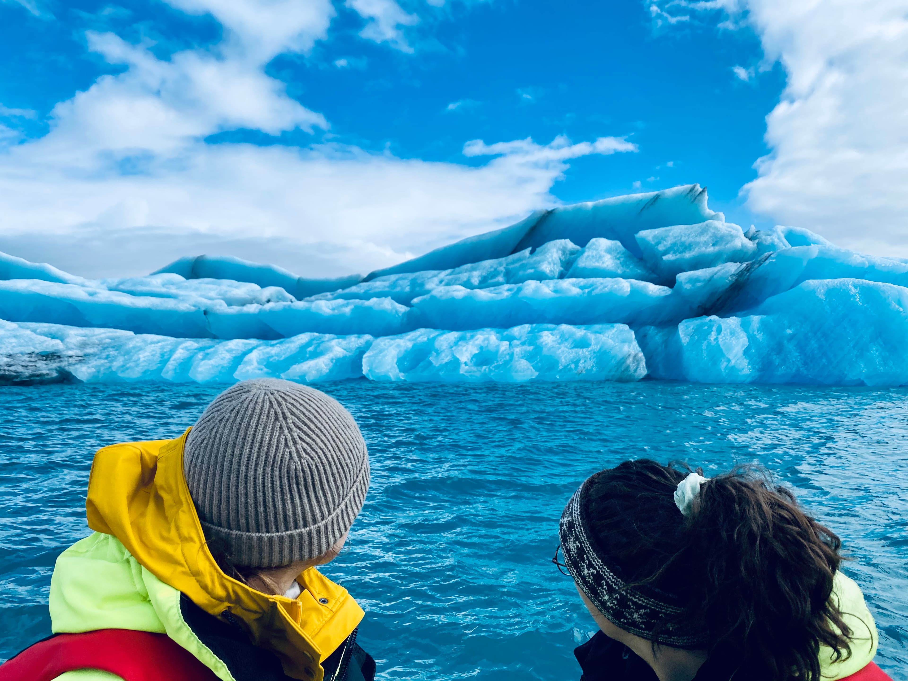 Katie and friend admire a large iceberg against a backdrop of calm, icy waters.