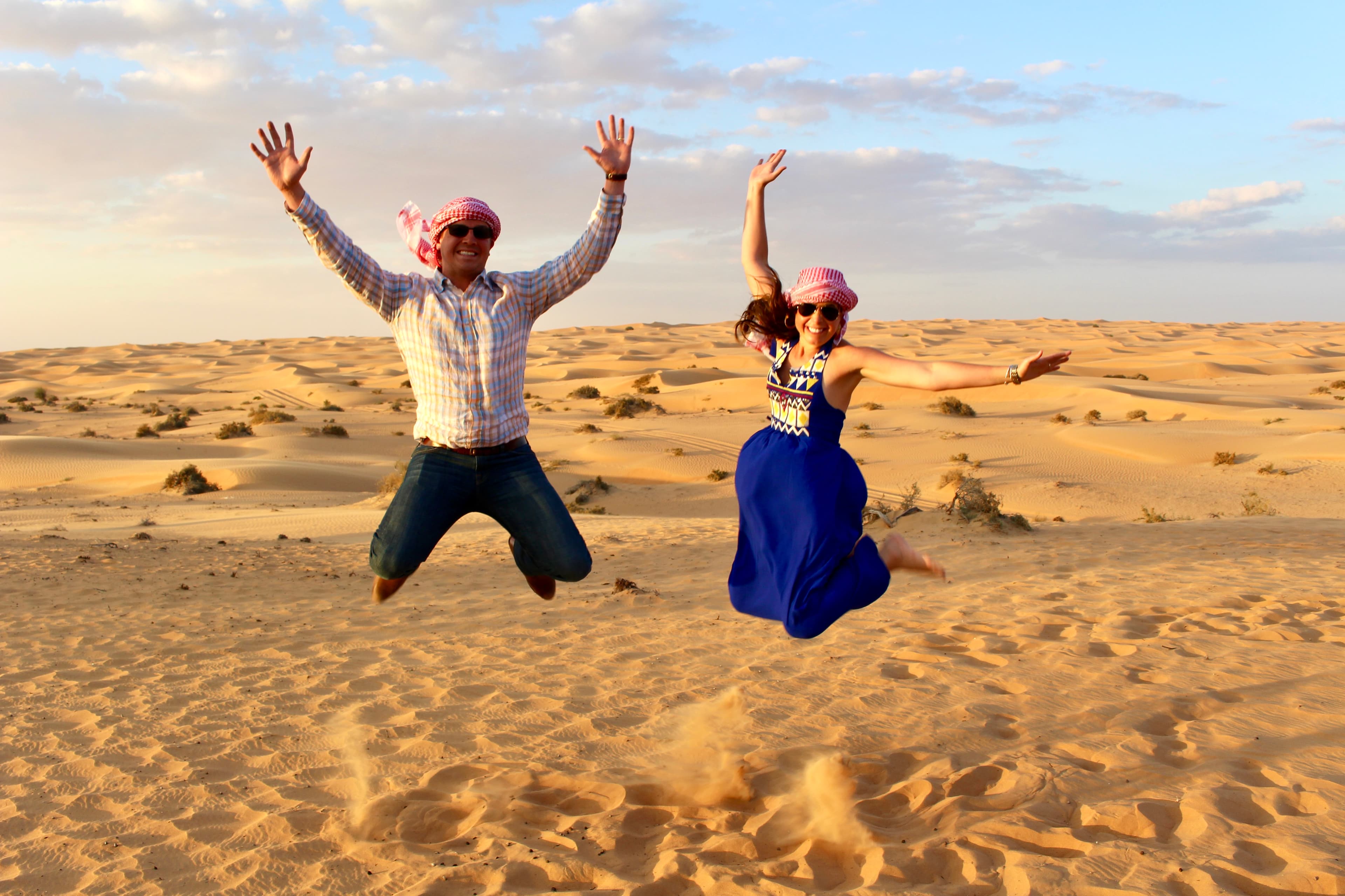 Advisor and partner wearing scarves around their heads and jumping in the air in a vast desert