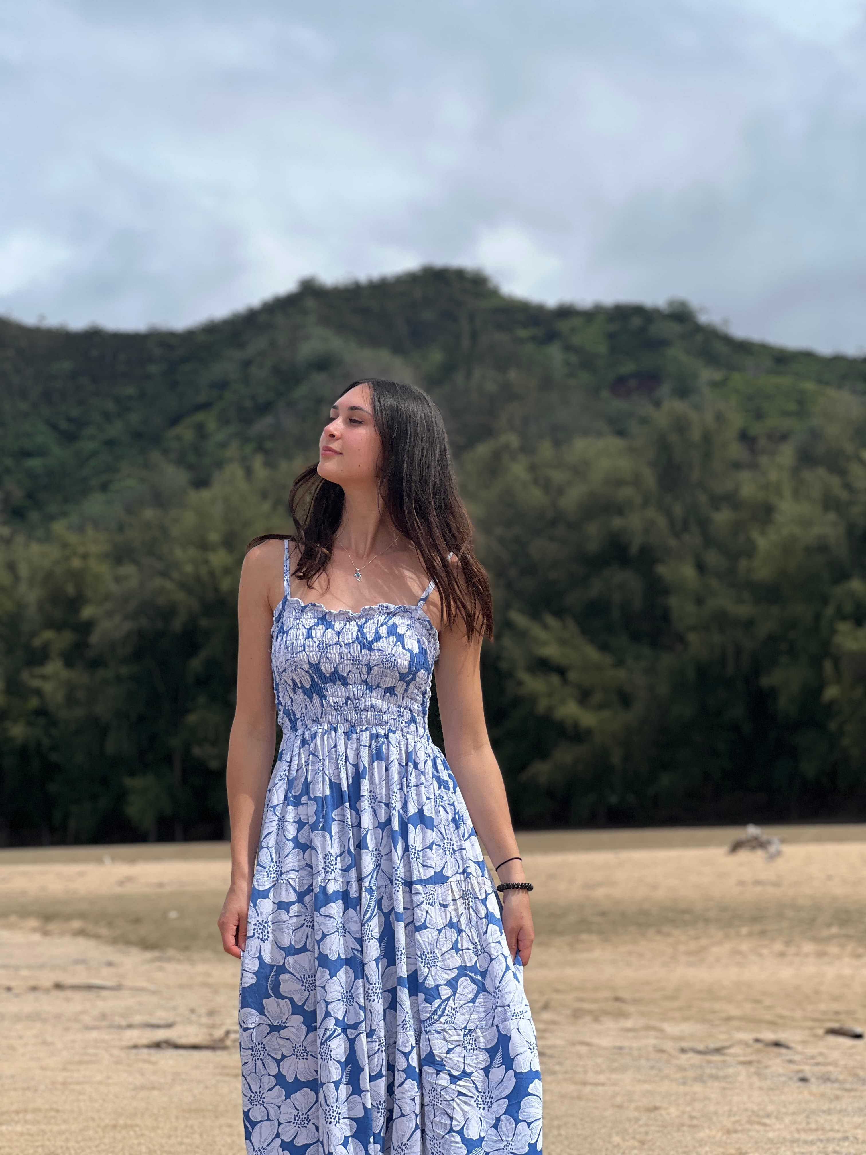 Advisor in a long blue and white dress posing on an empty beach lined with trees on a cloudy day