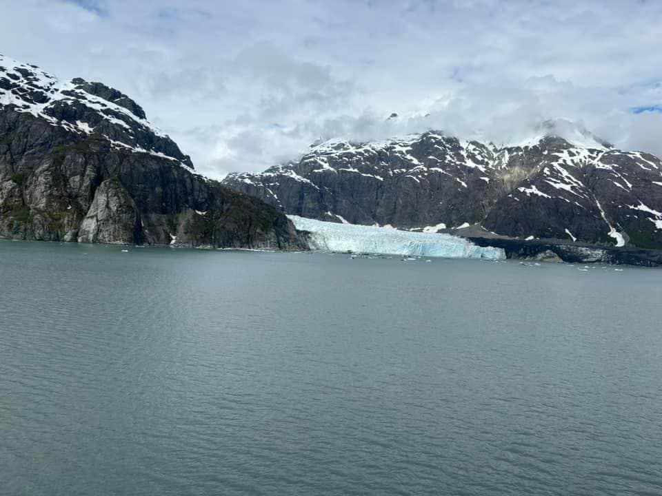 View of a glacial lake surrounded by large snowy mountains on a cloudy day