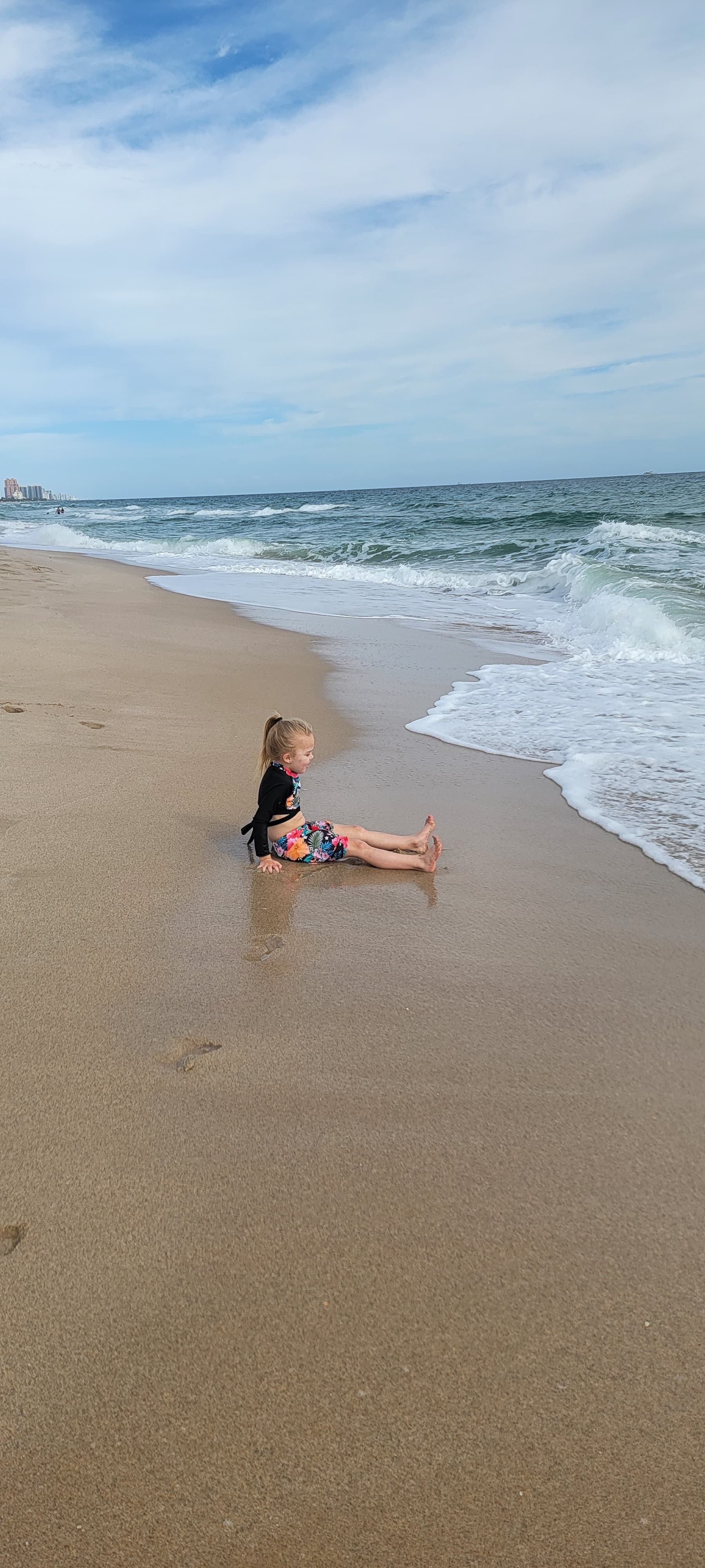 A child sitting on the beach watching the waves wash ashore