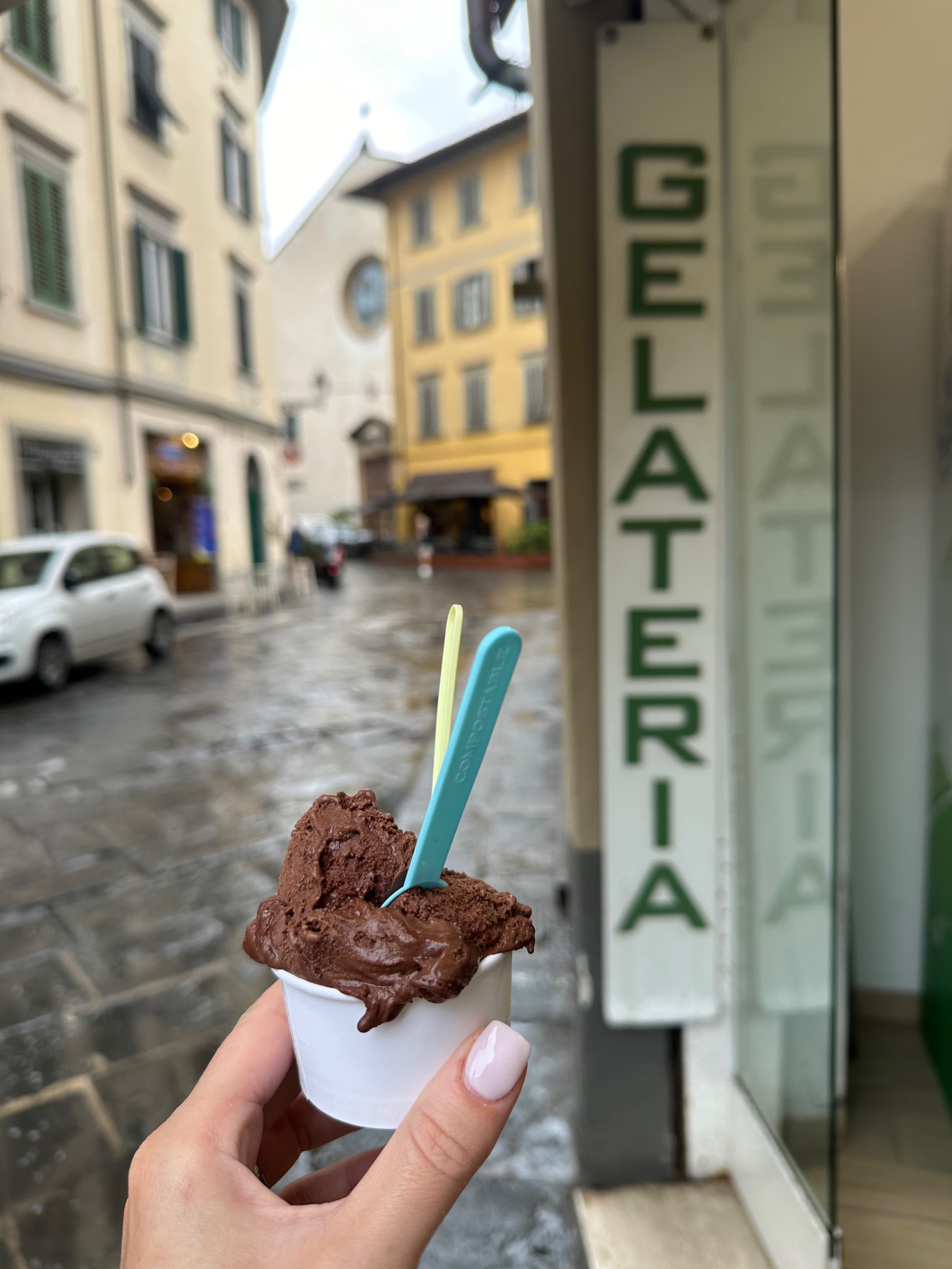Hand holding a small chocolate gelato outside the shop on a rainy day