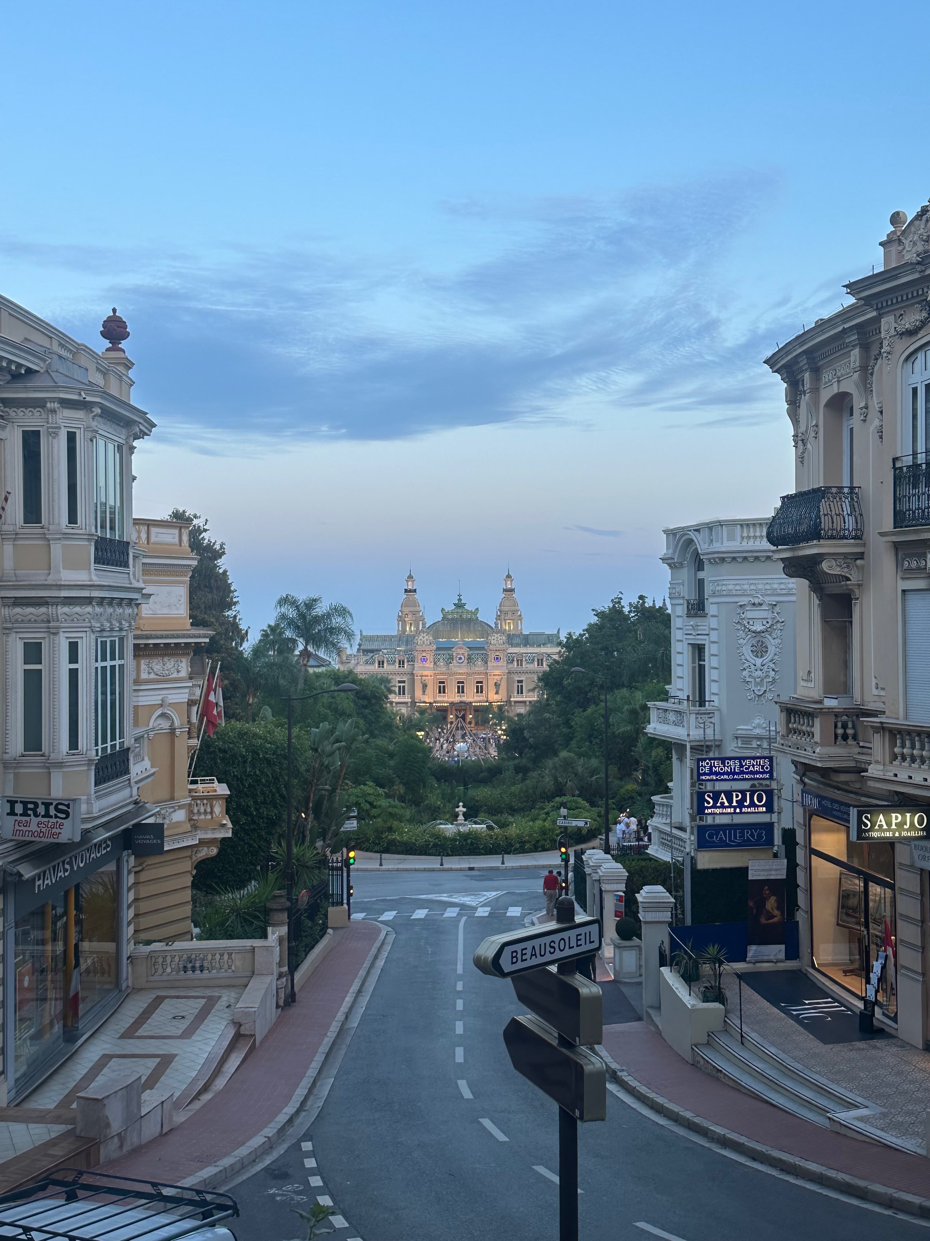View of an empty road at dusk with a beautiful building surrounded by trees in the distance