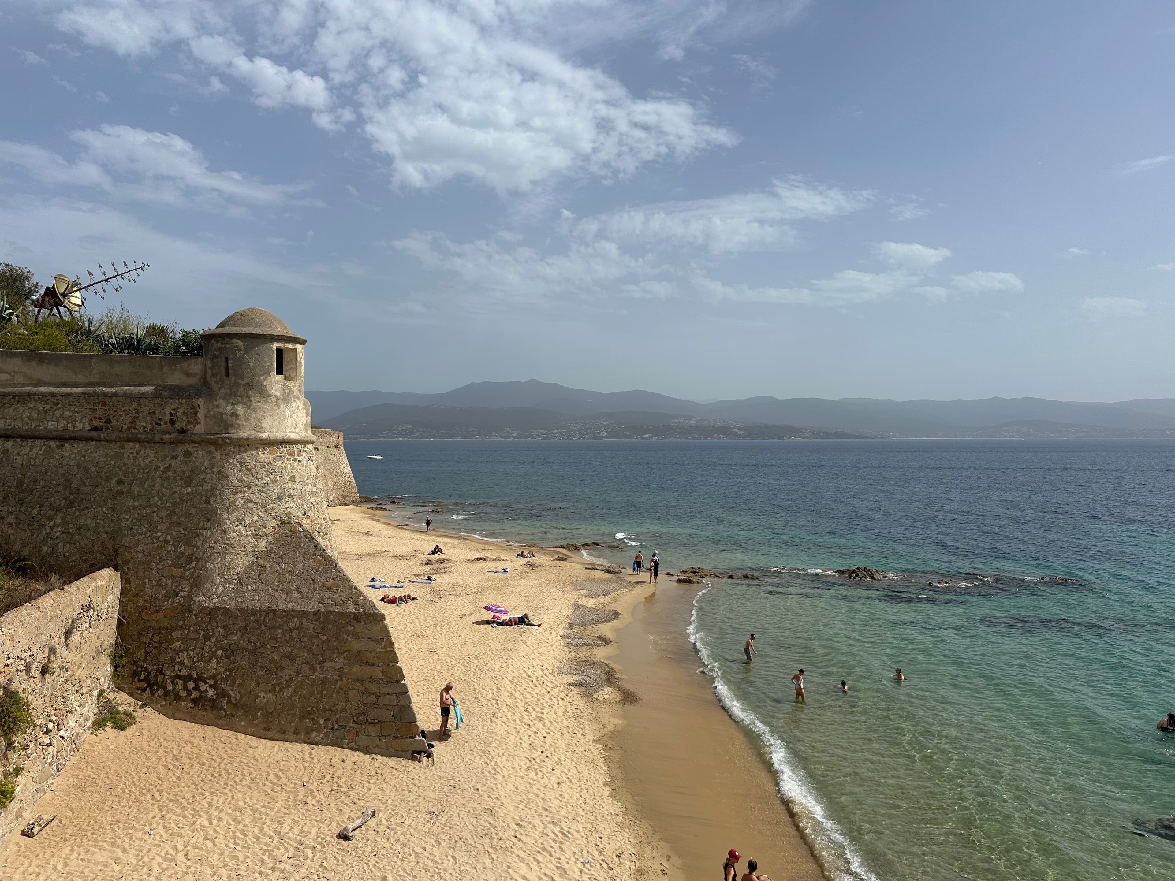 Aerial view of a seaside fort and beach with a few people swimming below