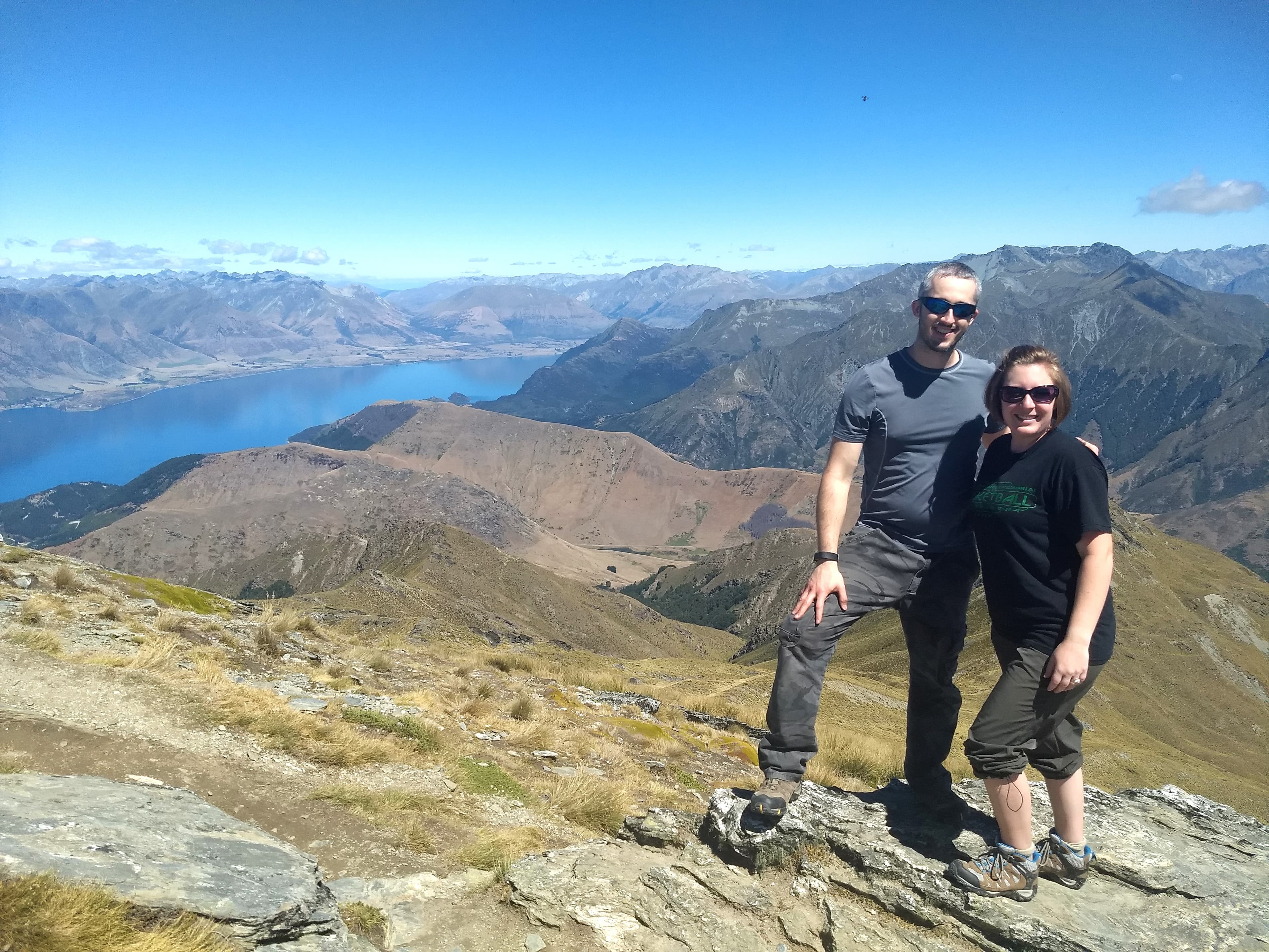 Chelsea and partner posing on top of a mountain during the daytime.