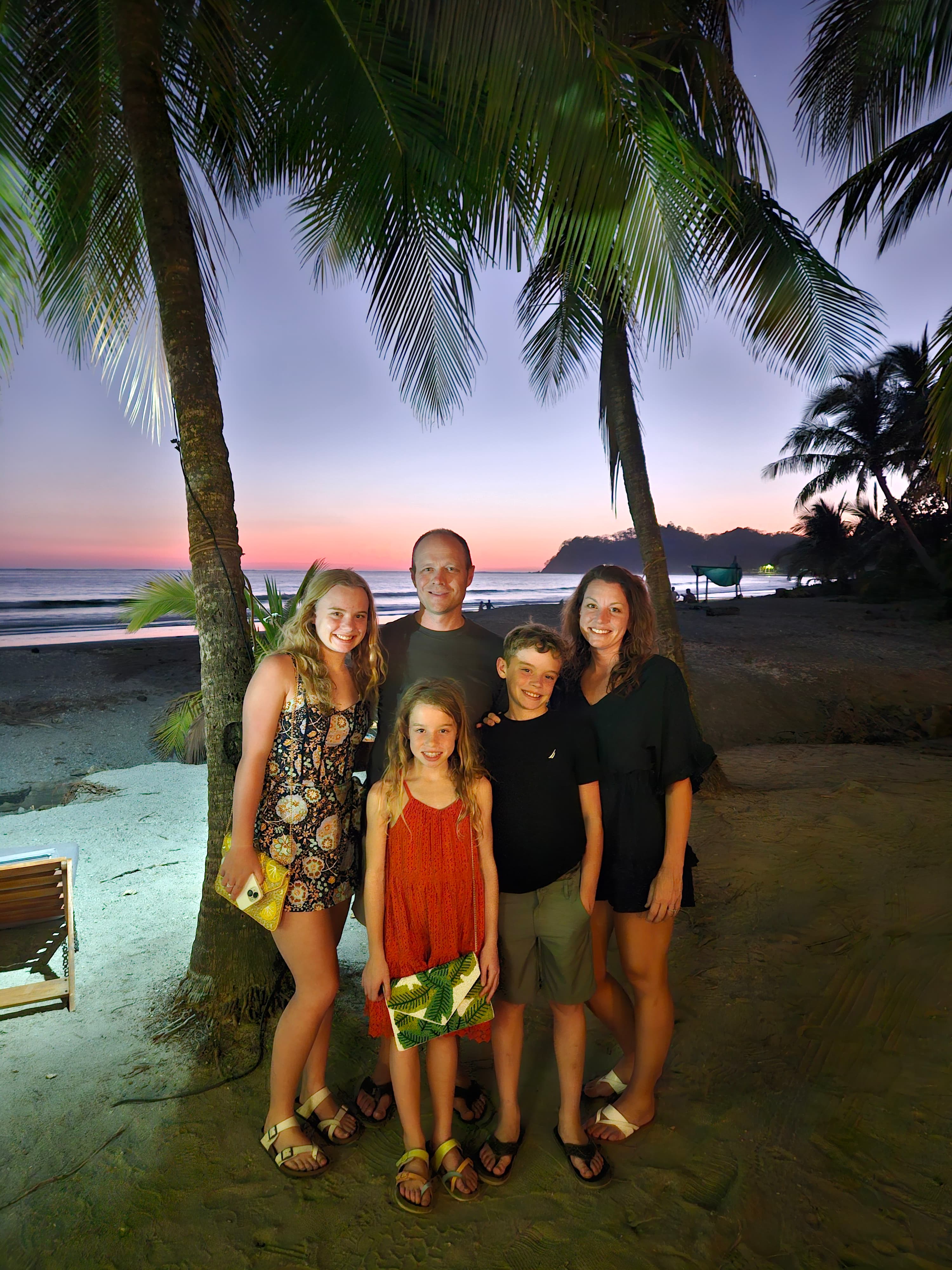 Advisor and family posing together underneath a palm tree on the beach at sunset
