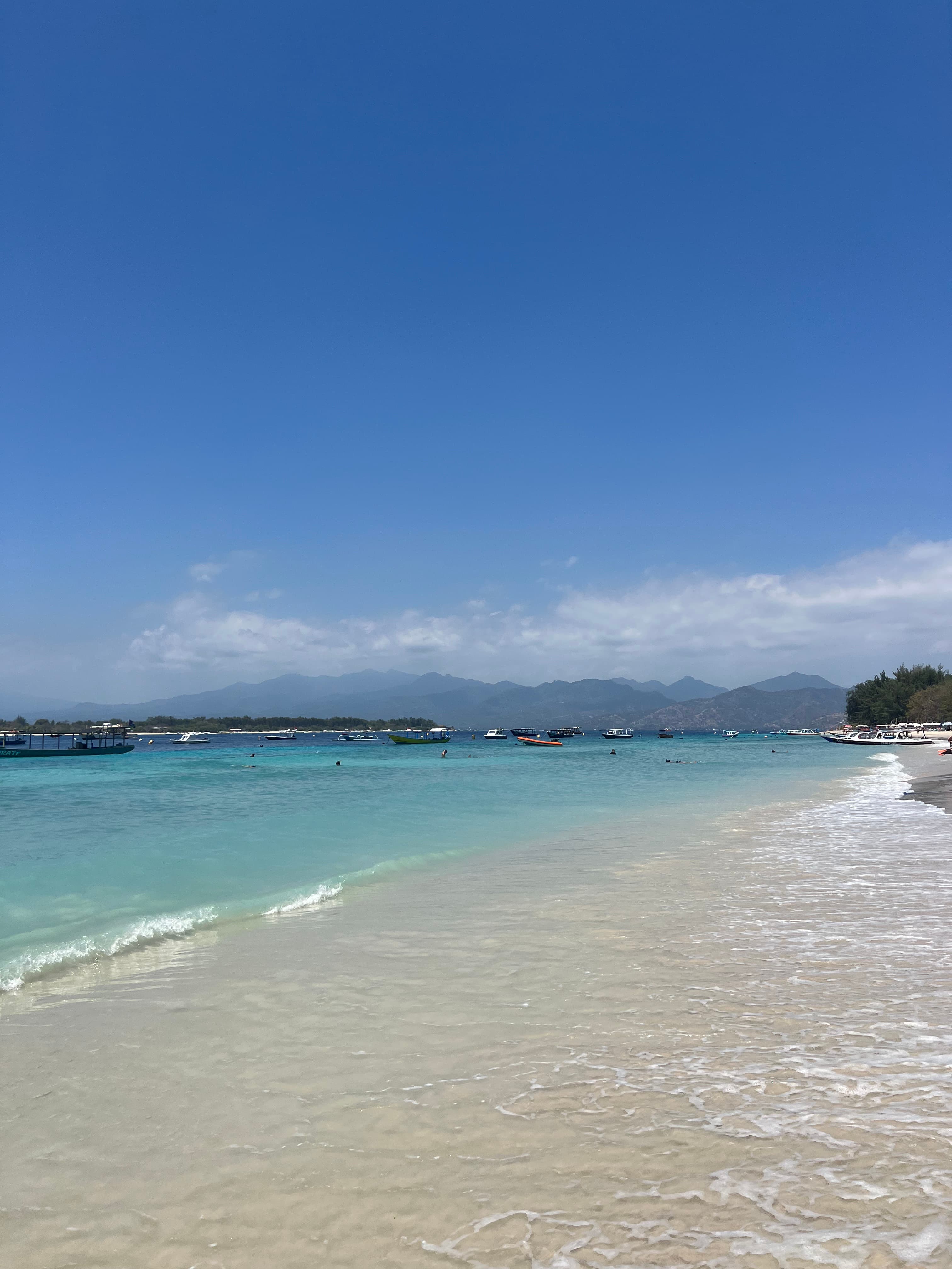 View of a calm white sand beach under clear skies
