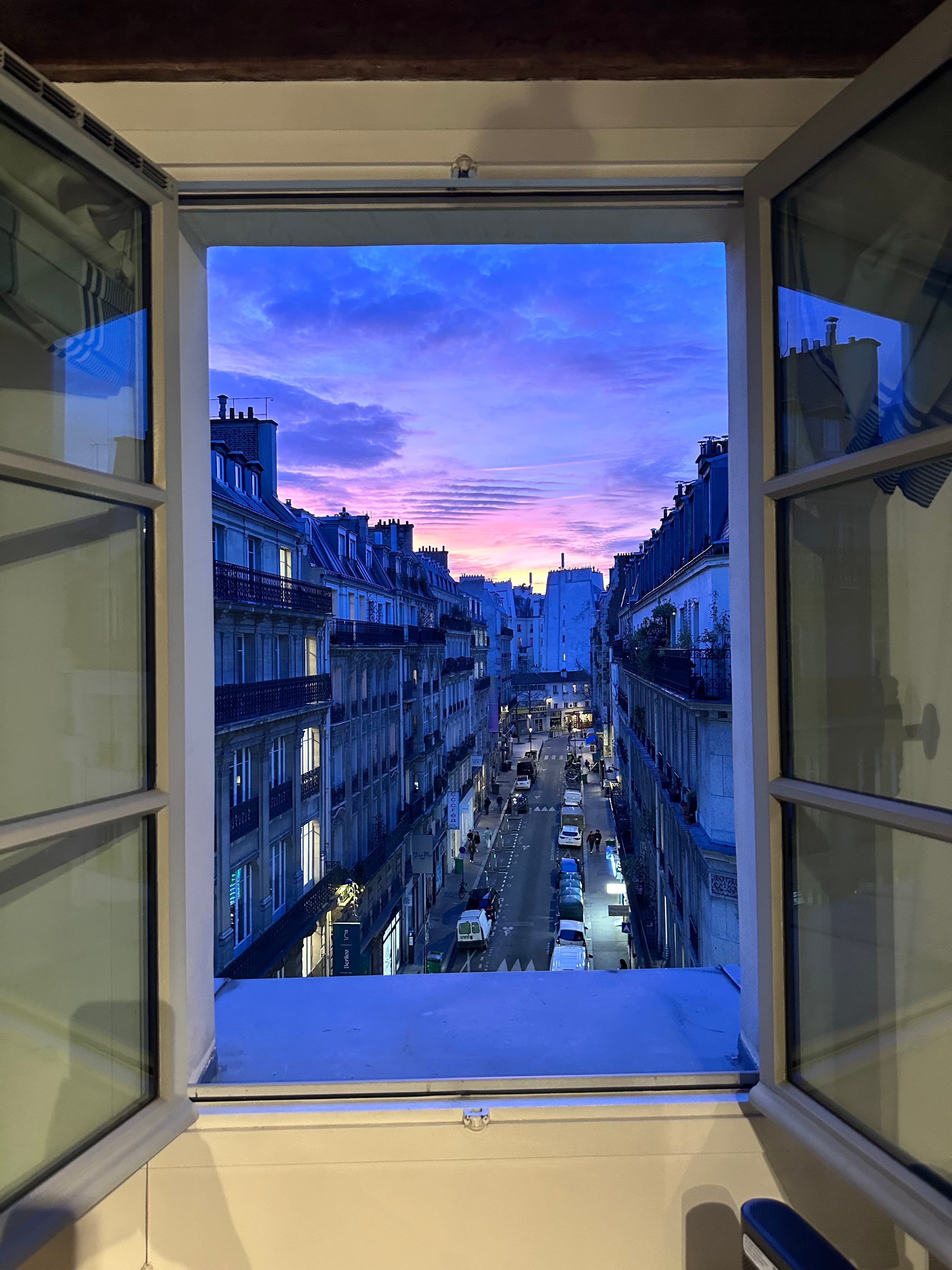 A window of a room looking out on a busy city street during a purple sunset