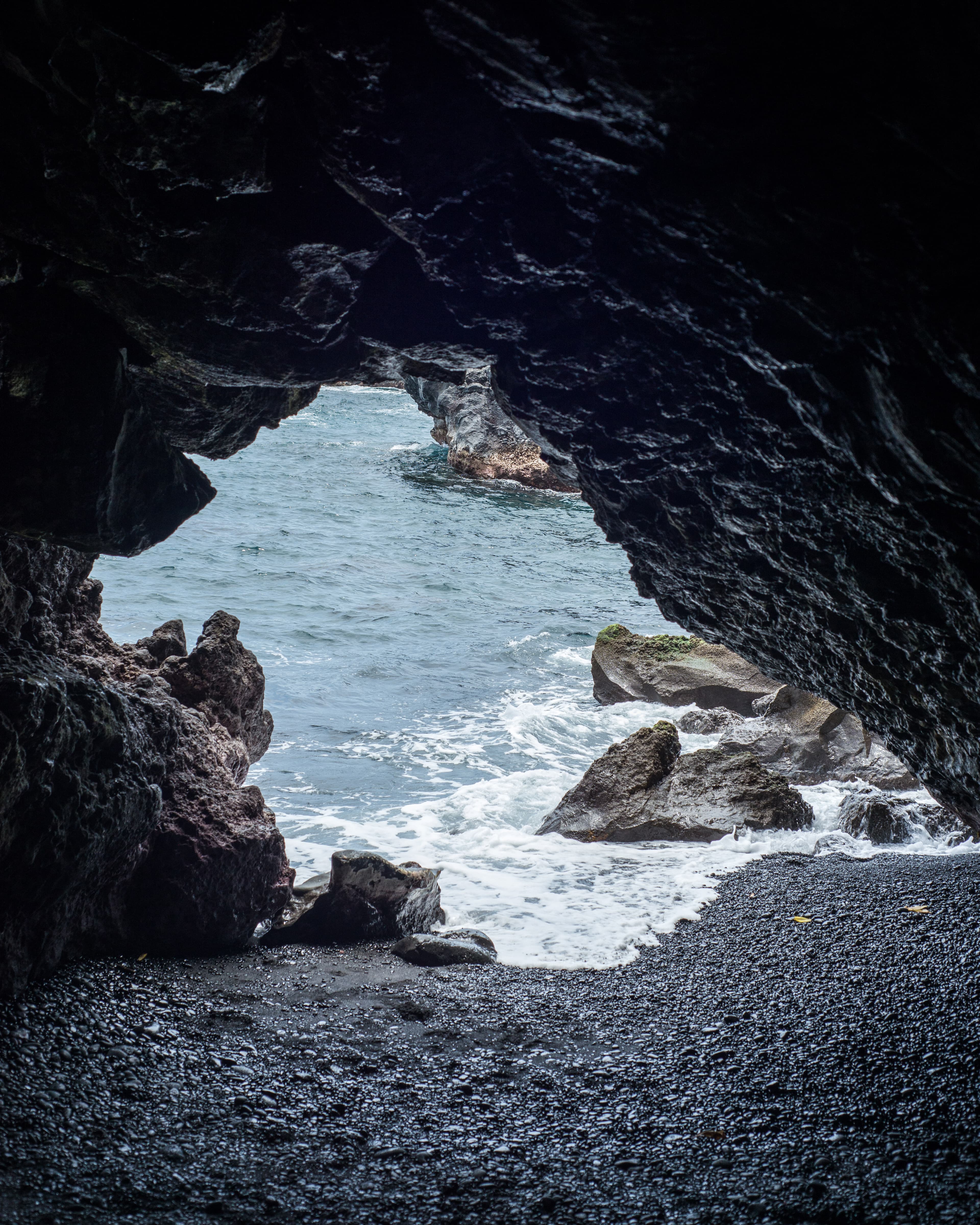 View of the mouth of a cave with the ocean and rocks visible in the sunlight