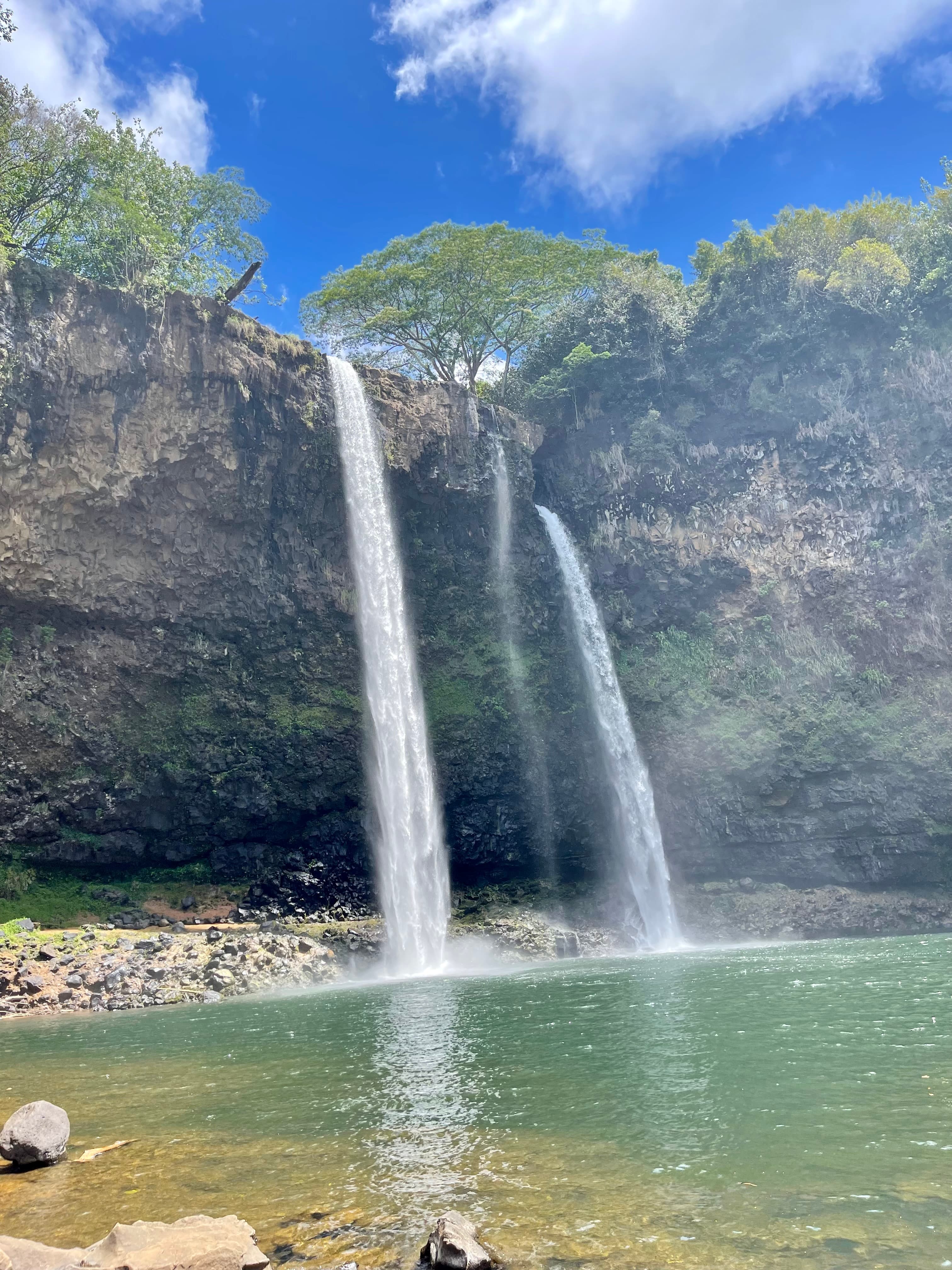 View of twin waterfalls pouring into a swimming hole surrounded by cliffs on a sunny day