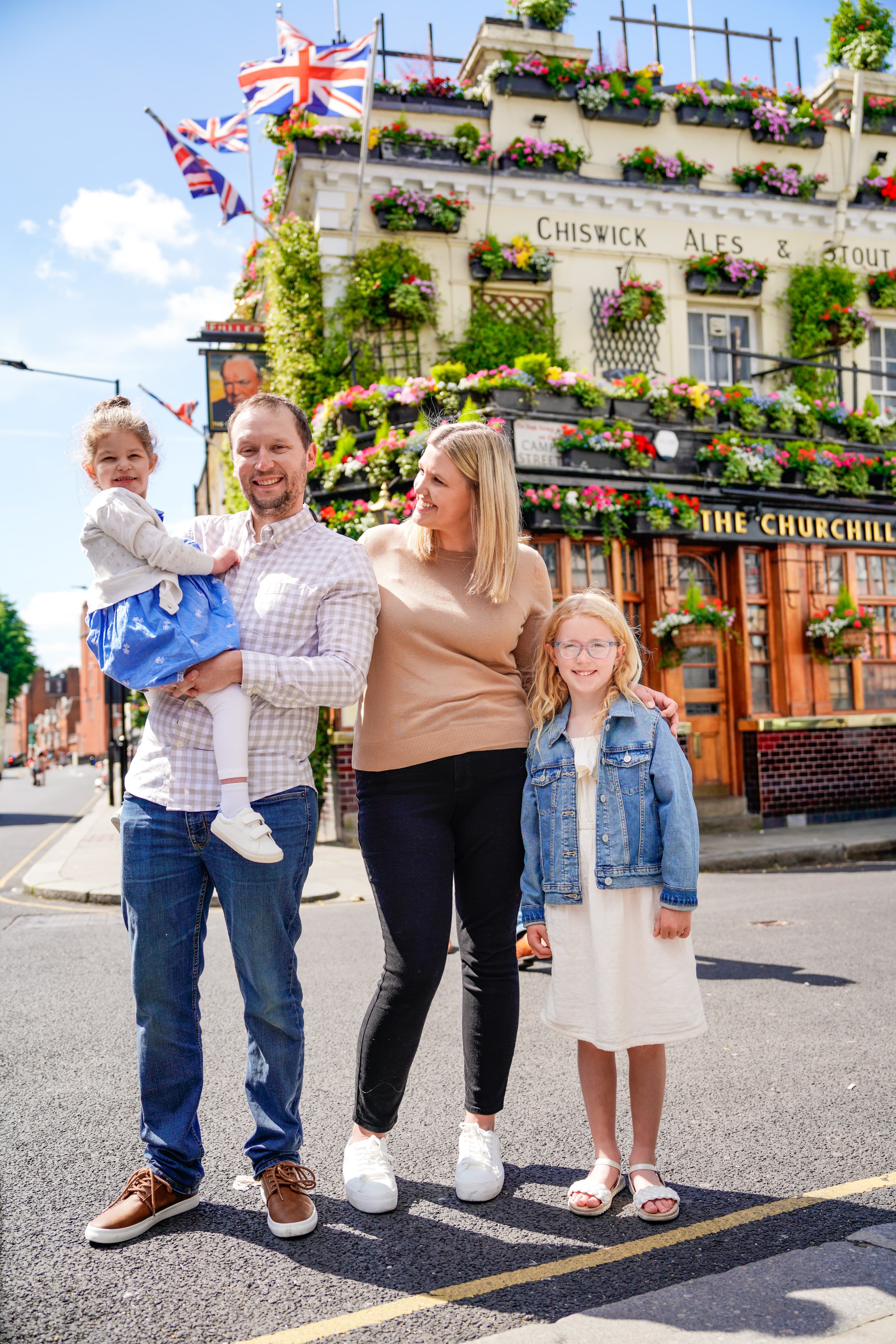 Advisor and family smiling on a sunny street corner with a pub decorated with flowers behind them