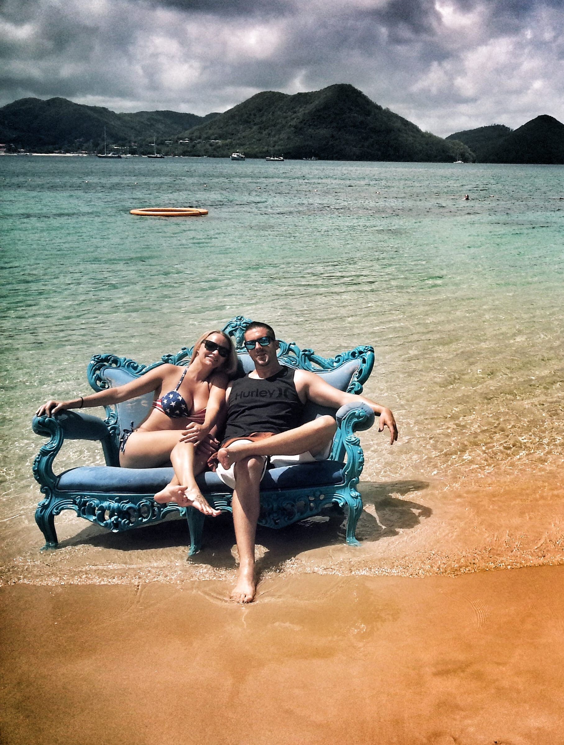 Advisor and partner sitting on a blue couch in shallow ocean water with mountains visible across the bay