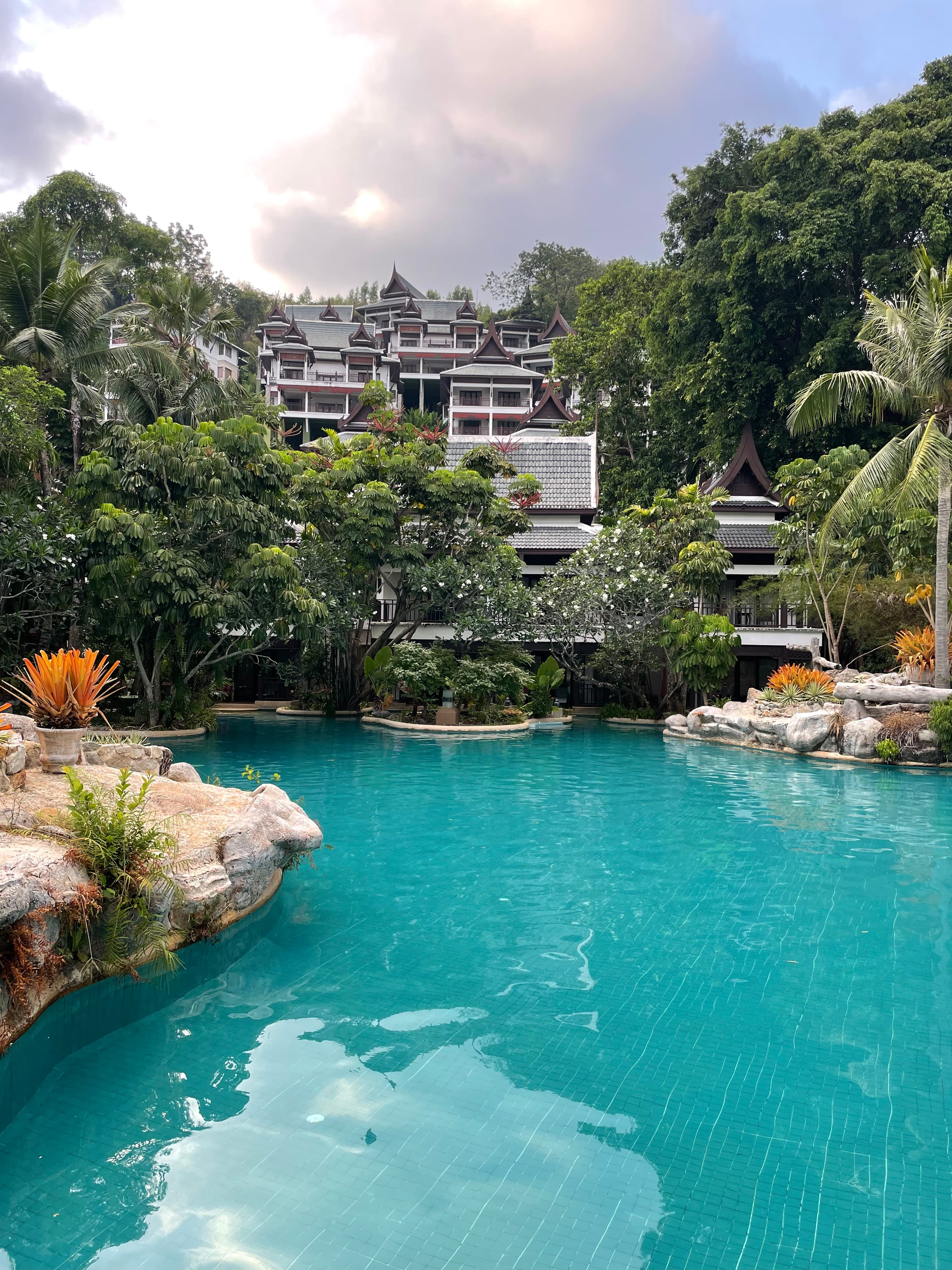 View of an empty resort pool surrounded by lush vegetation and hotel buildings