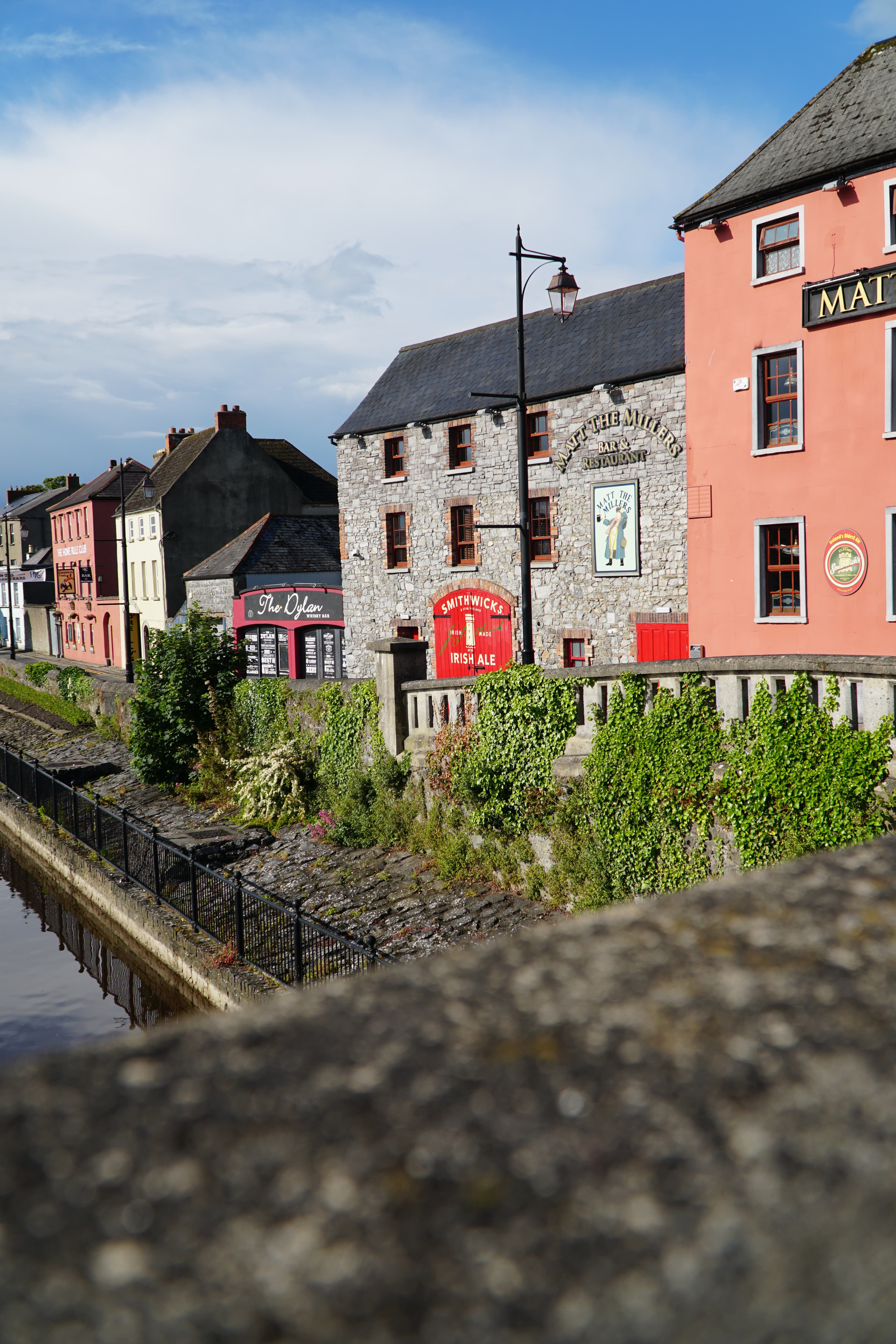 View of small quaint homes along a river lined with plants under sunny skies