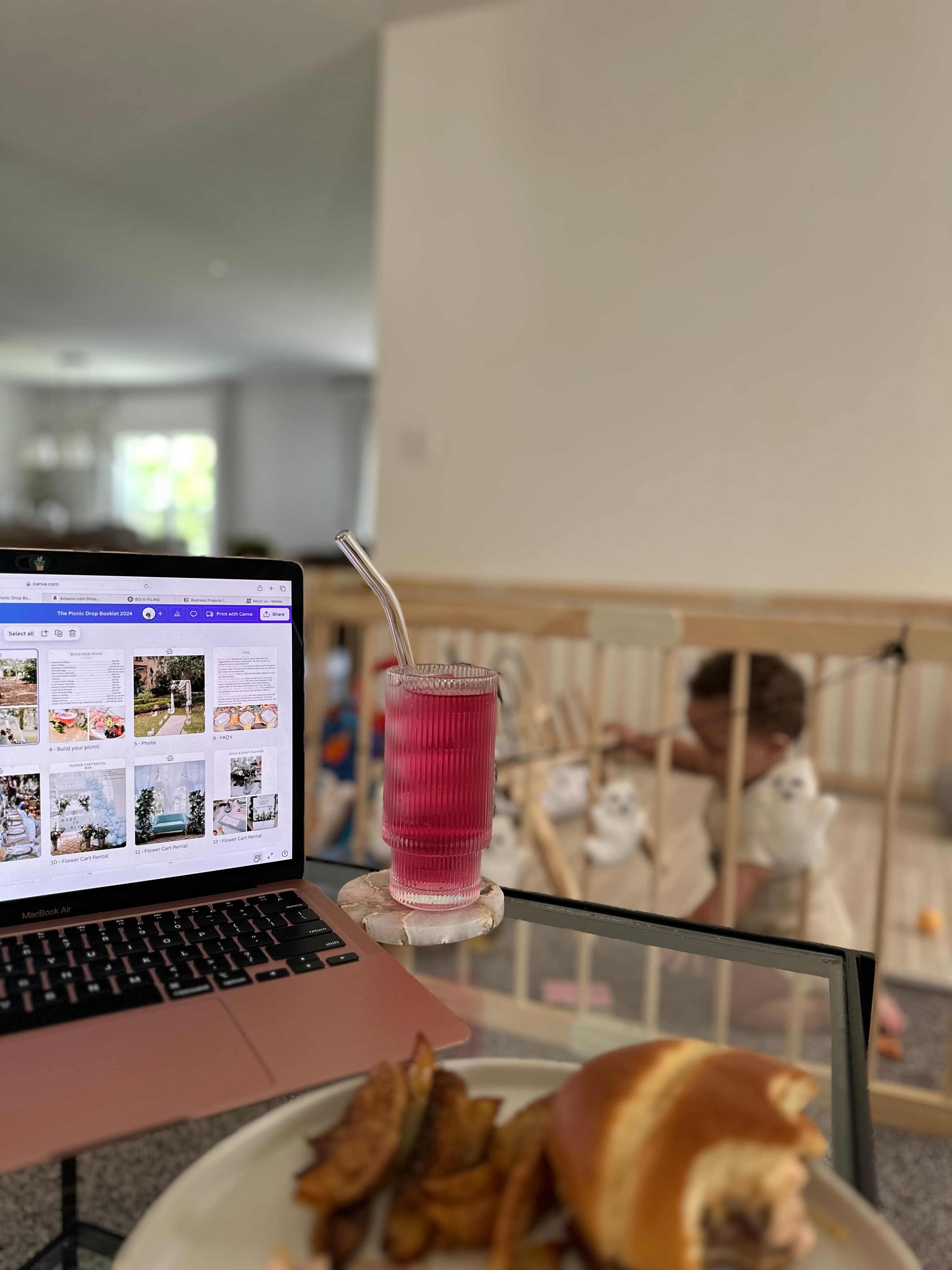 A plate of food and pink beverage on a glass table next to a pink laptop
