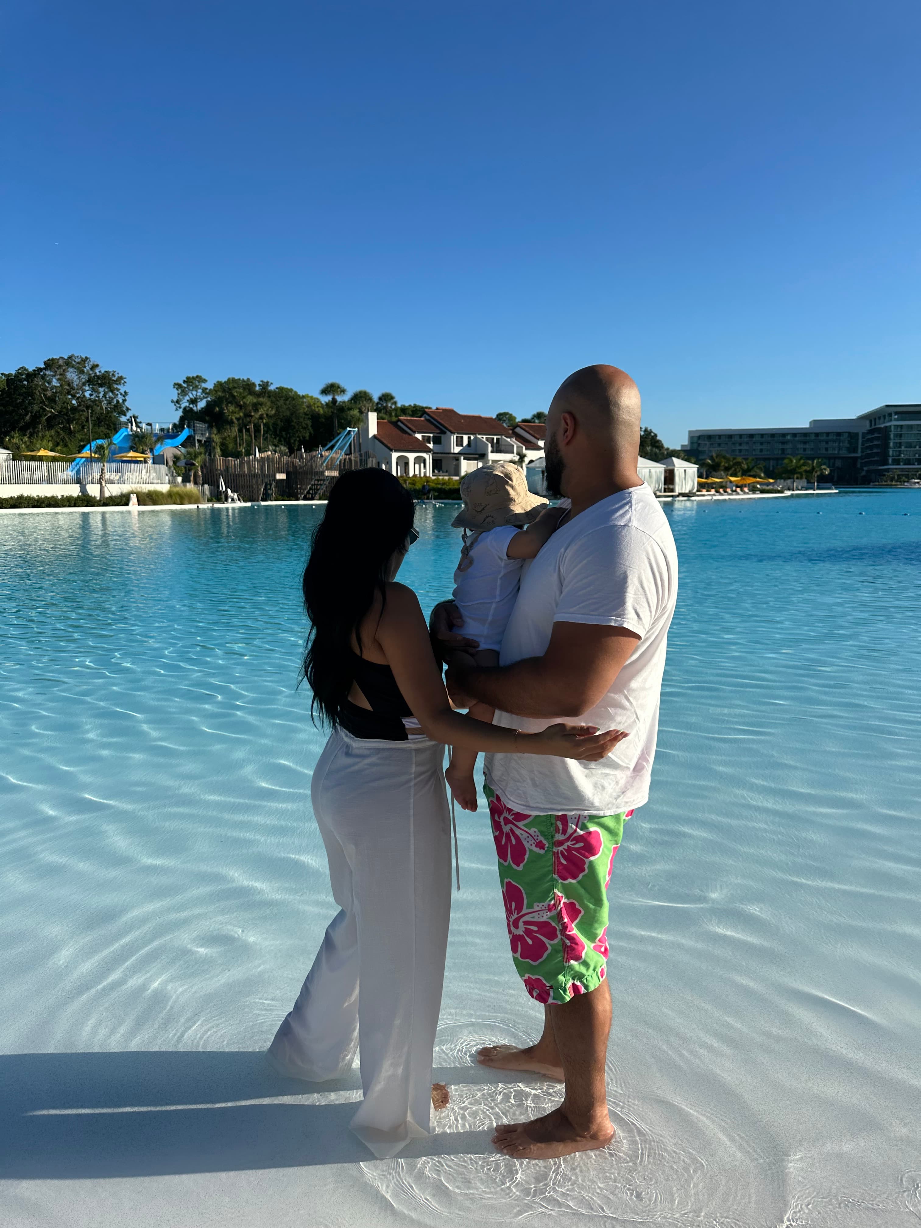 Advisor standing in shallow clear water with her partner and child under clear skies