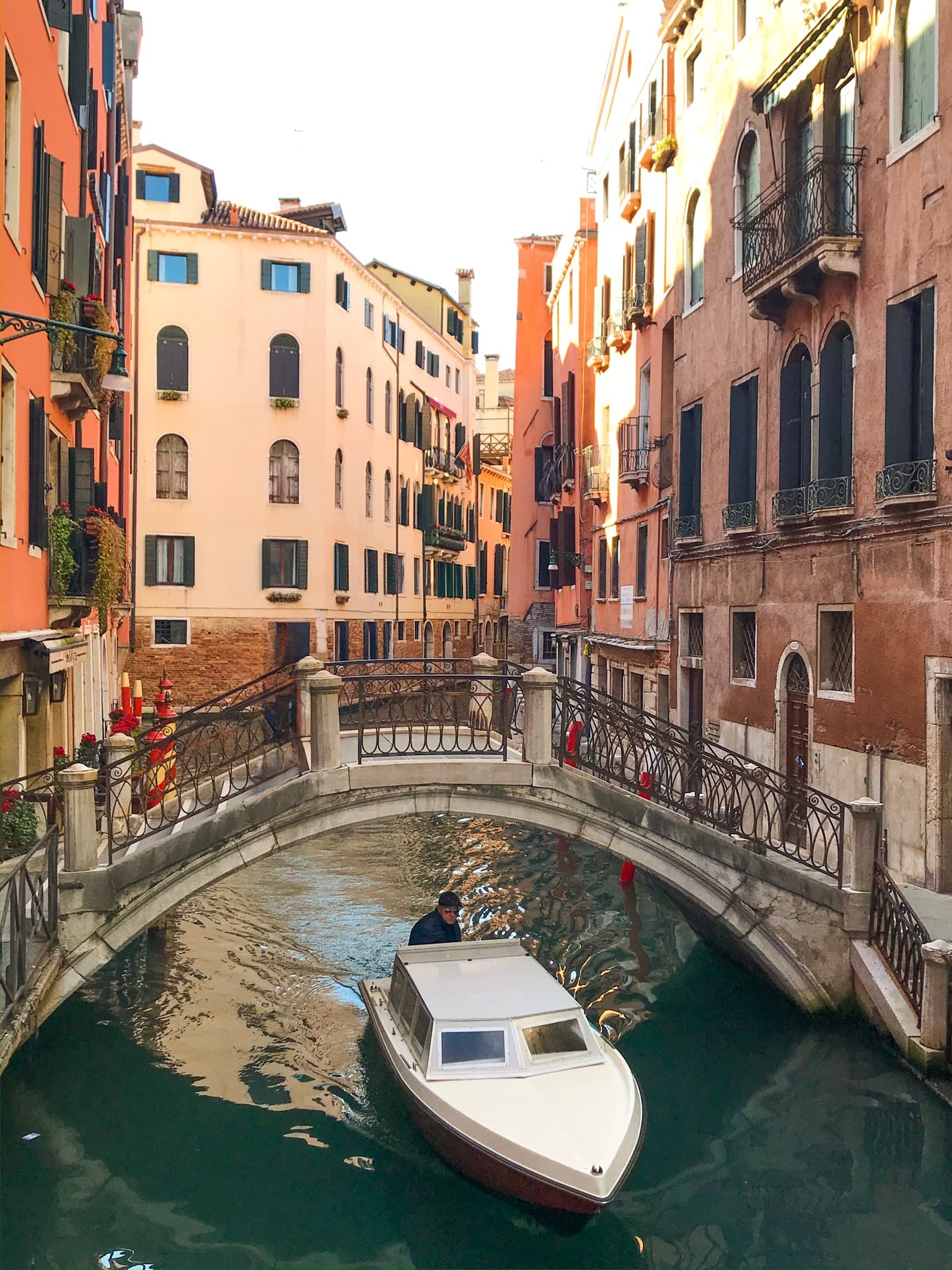 View of a small white boat sailing underneath a bridge on a canal in Venice, Italy