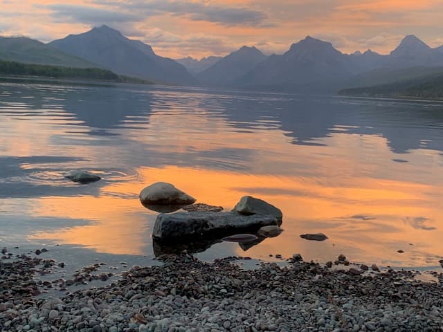 View of a glassy lake reflecting an orange sunset with mountains in the distance