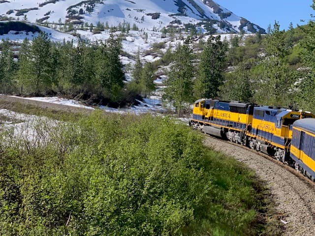 View of a blue and yellow passenger train on a track through snowy mountains