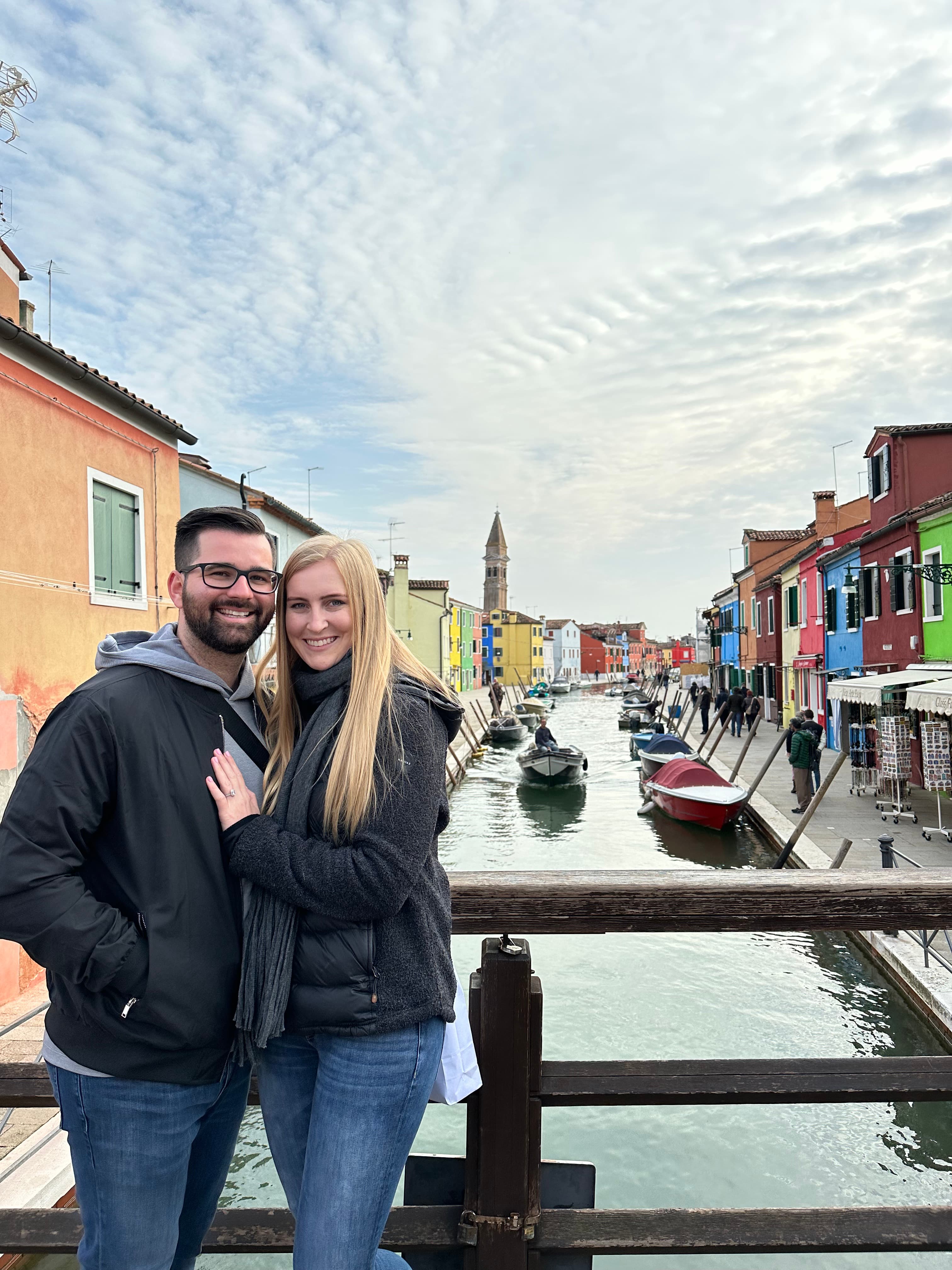 Advisor and partner smiling side by side on a wooden bridge over a canal lined with colorful buildings