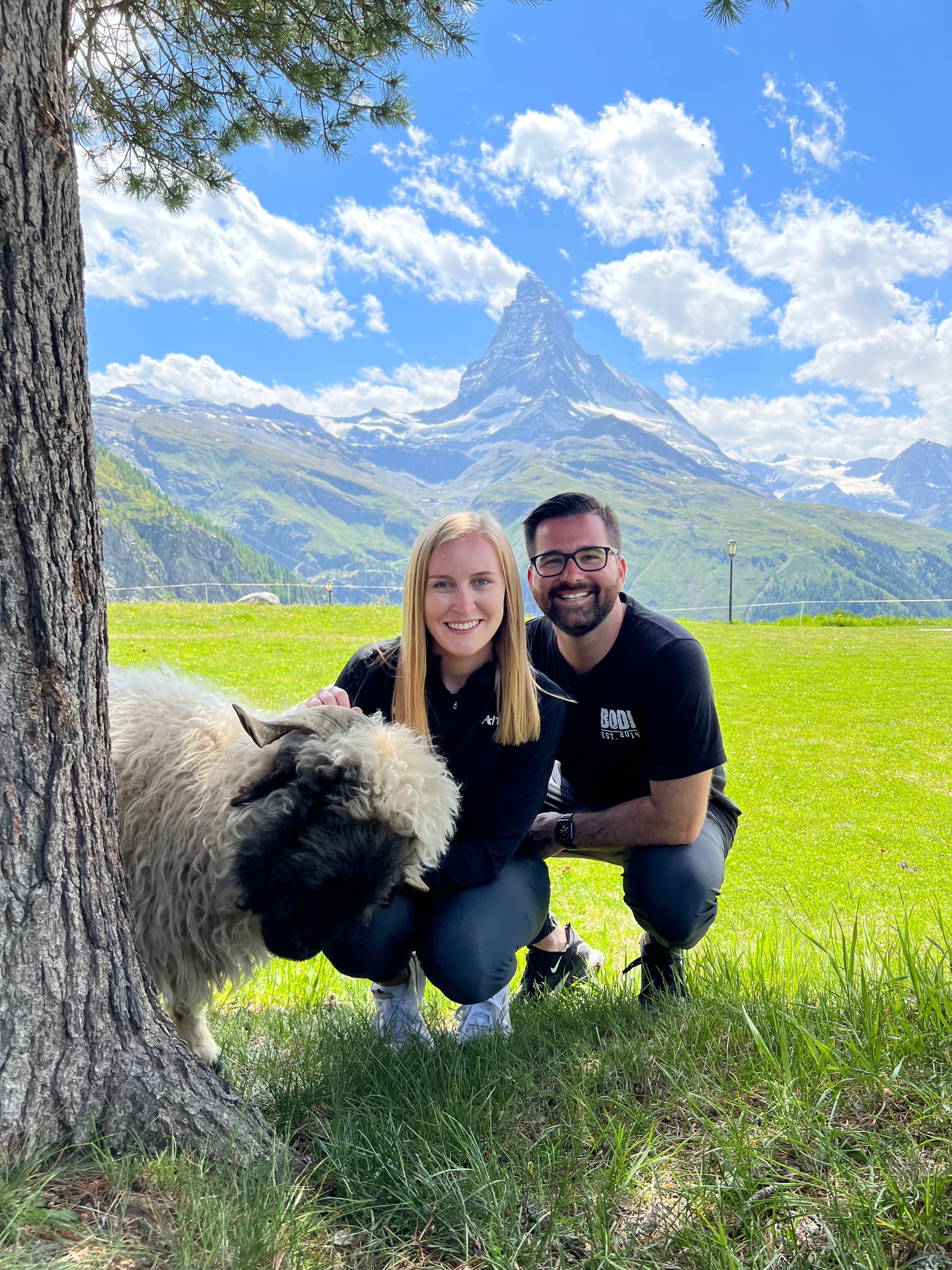 Advisor and partner posing in a beautiful green field with a sheep peeking out from behind a tree