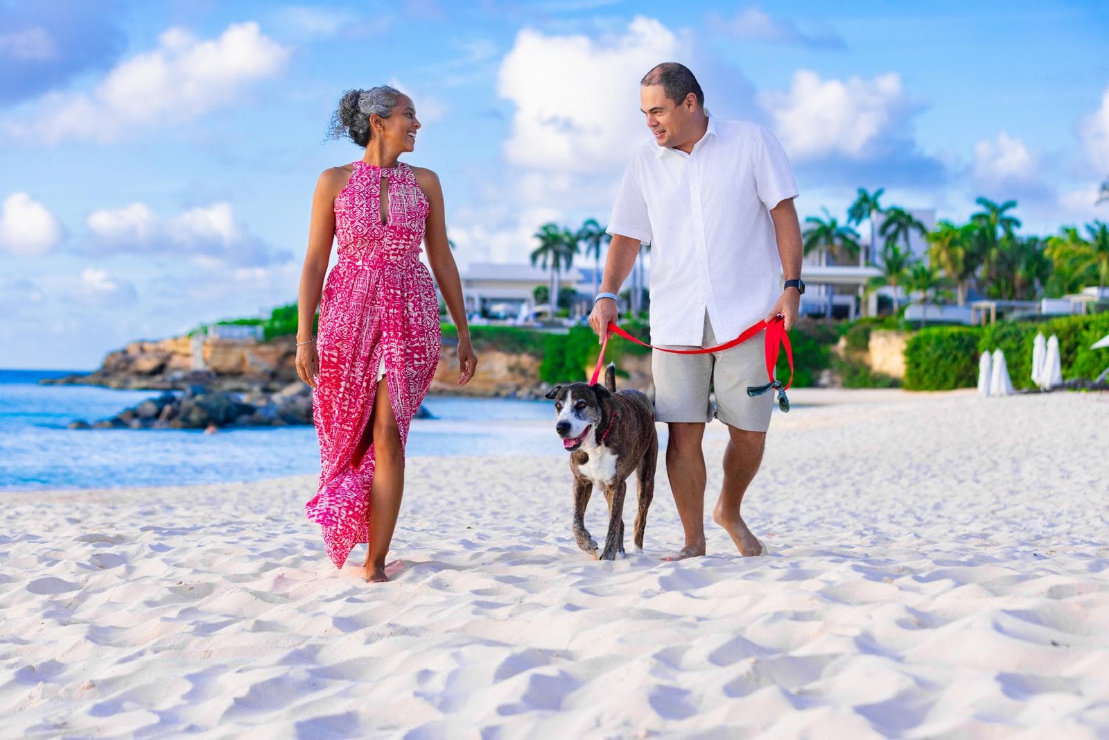 Advisor and partner walking with their dog on a white sand beach under sunny skies