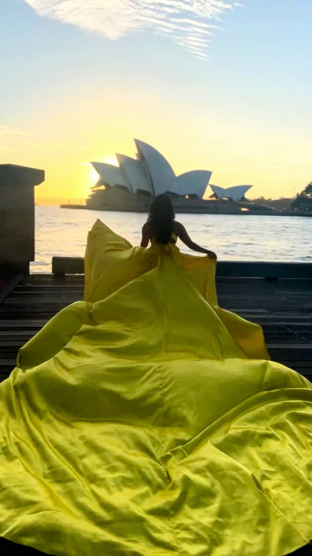 Advisor in a long yellow-green dress with the Sydney Opera House visible across the water at sunset