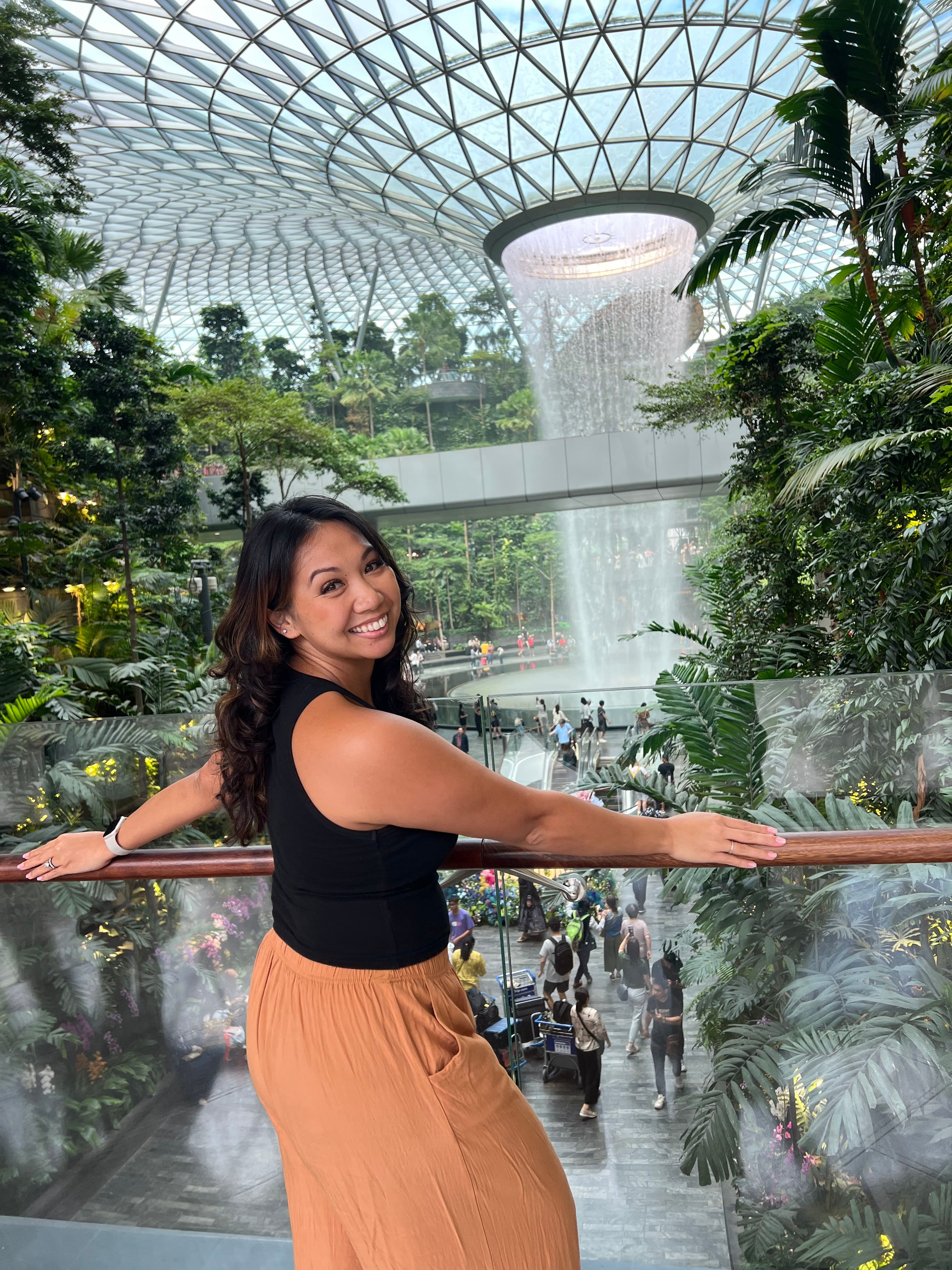 Advisor smiling inside the Singapore airport with the famous circular waterfall and plants in the background