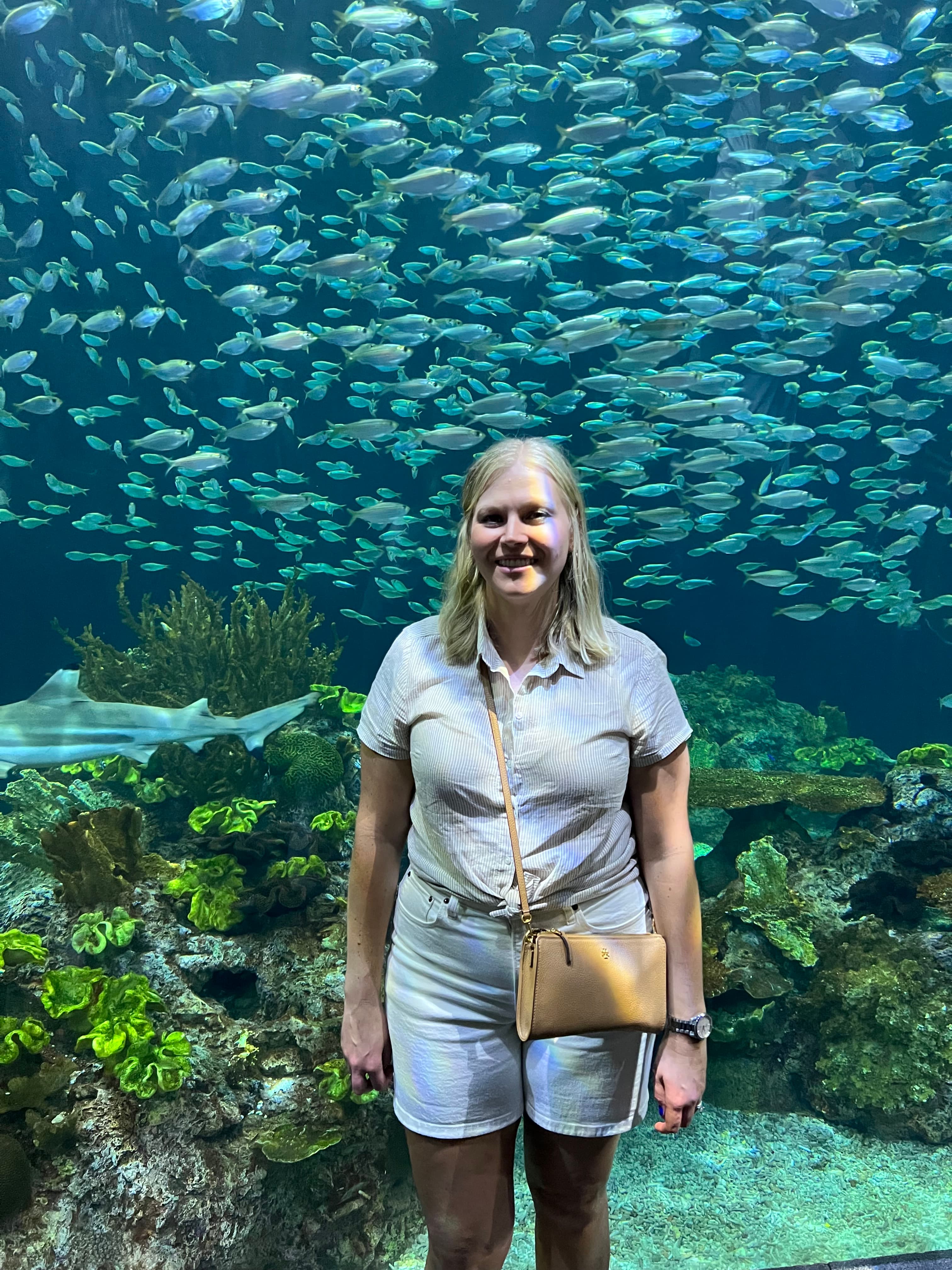 Advisor posing in front of a large aquarium tank with hundreds of fish swimming behind her