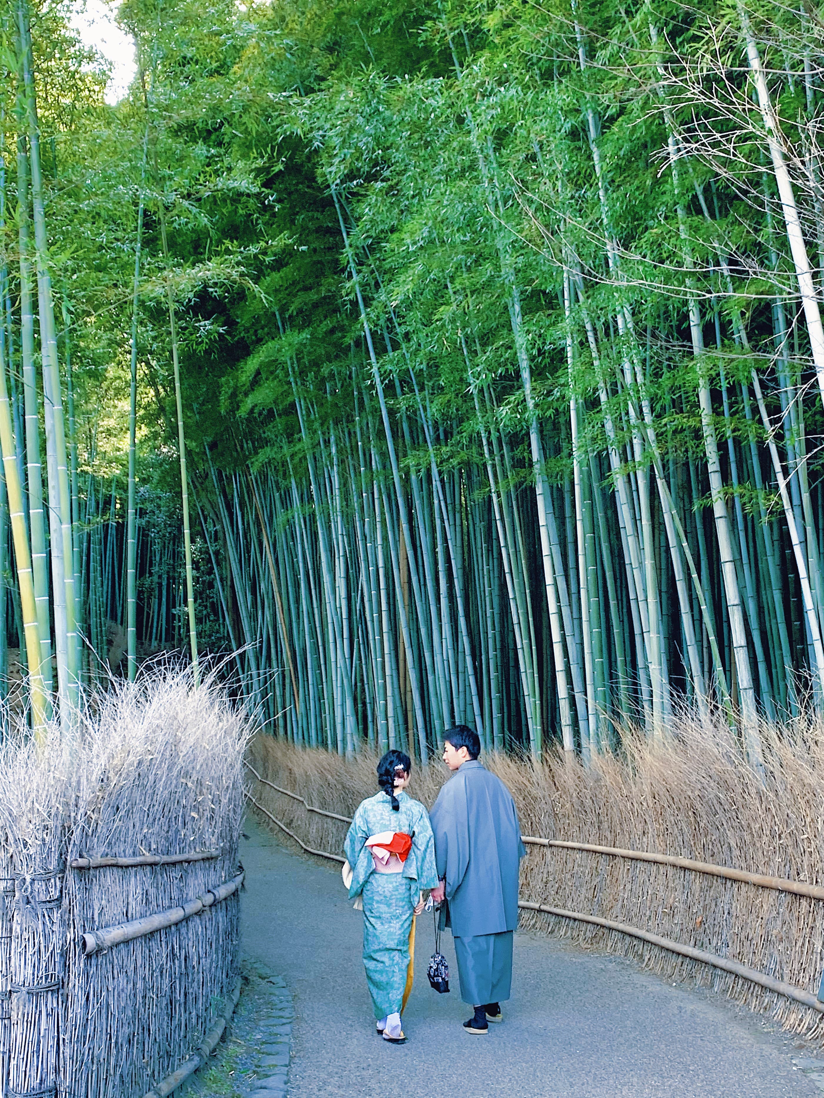 Two people walking through a forest wearing traditional Japanese clothing