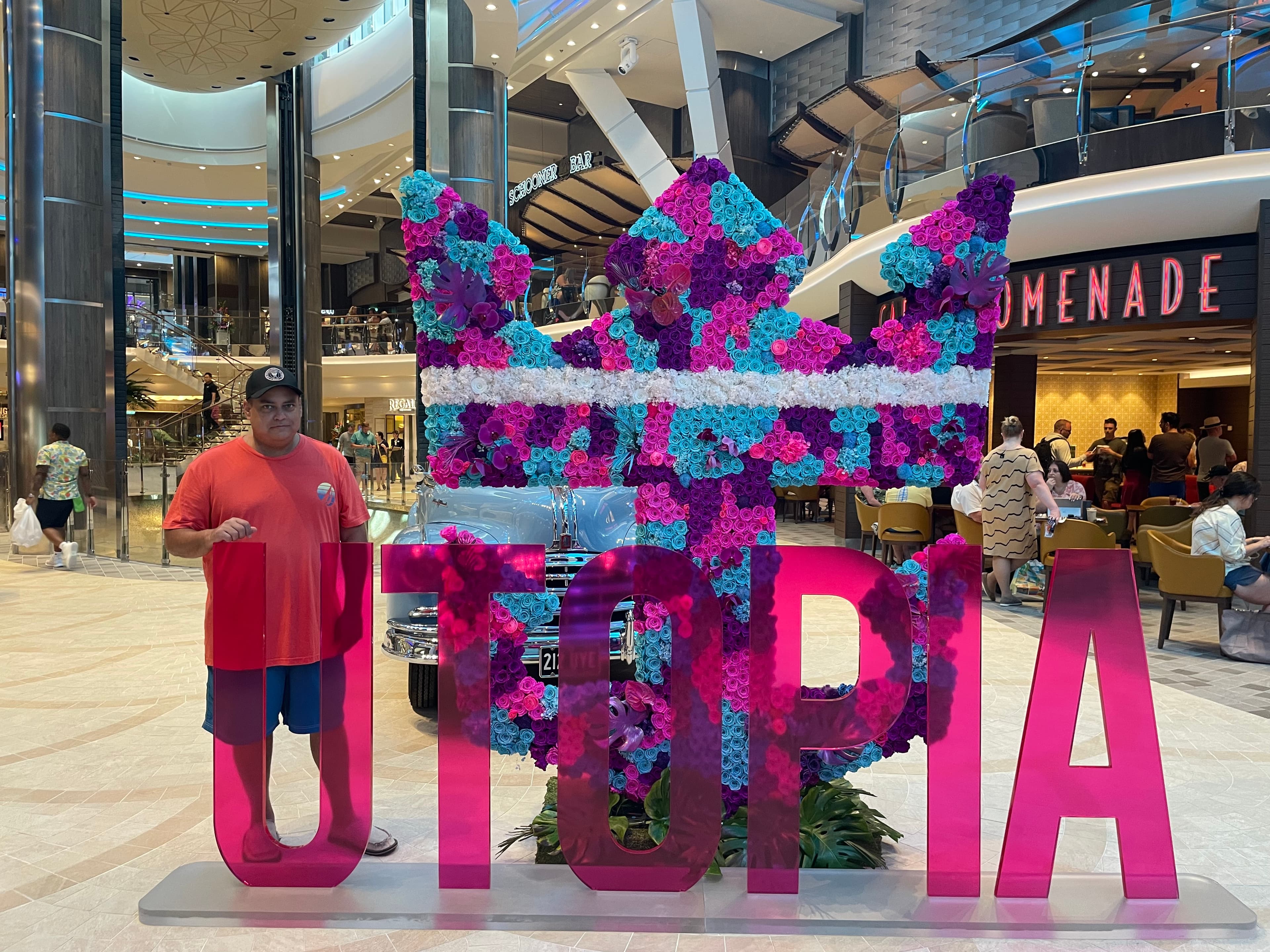 Advisor posing behind a pink sign with the letters spelling “UTOPIA” and a colorful flowery display