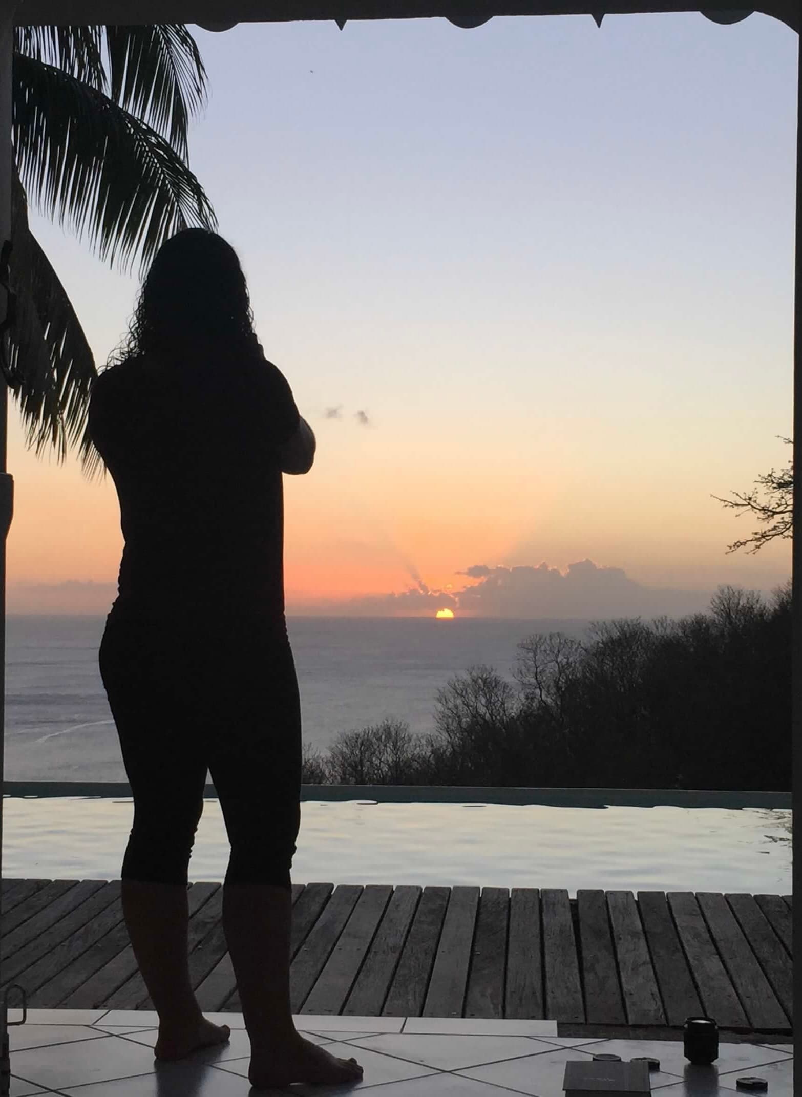 Advisor in silhouette looking out over the sea from a balcony at sunset