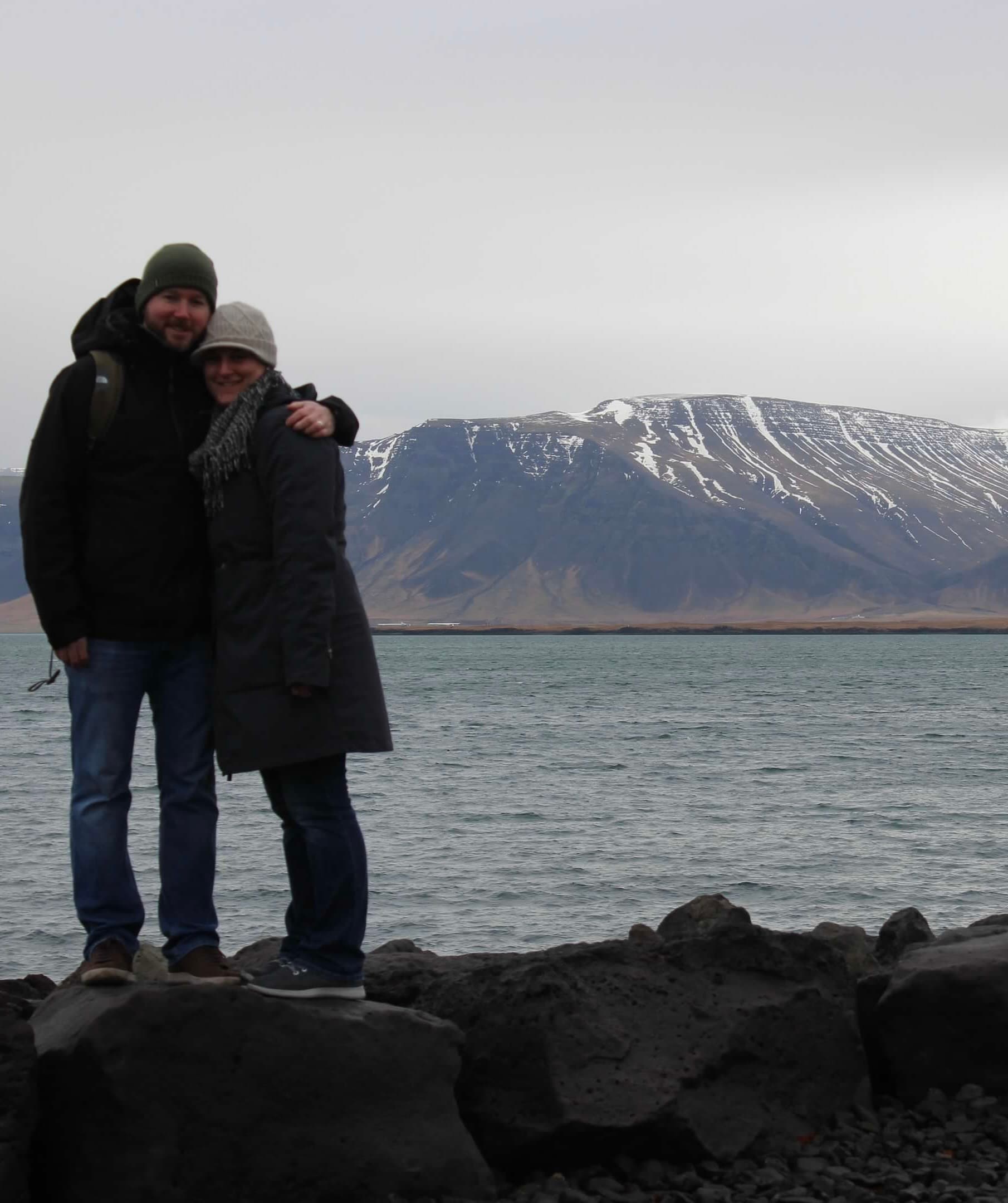Advisor and partner posing side by side by the sea with a snowy mountain range in the distance