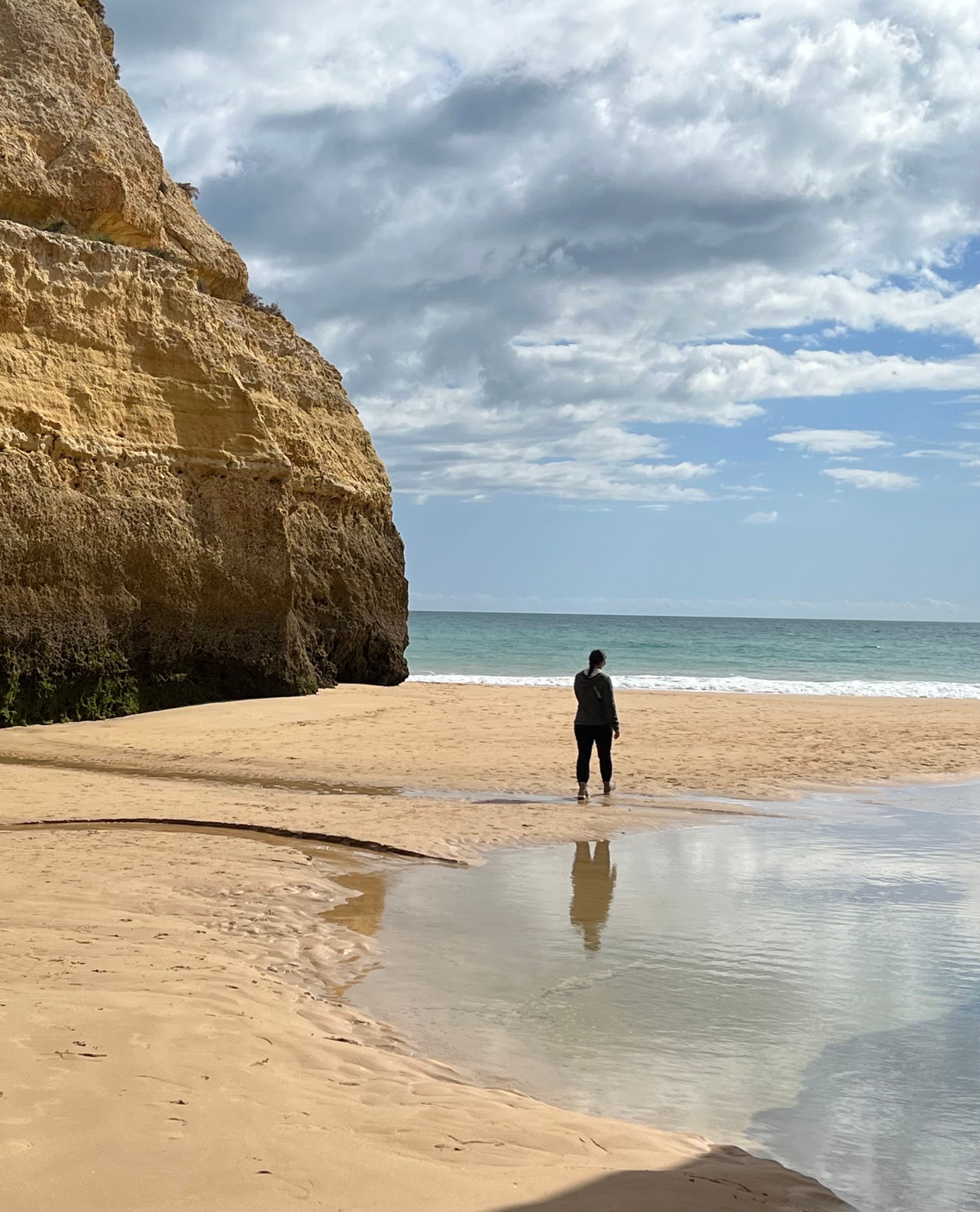 Advisor standing alone on the beach beside steep cliffs on a sunny day